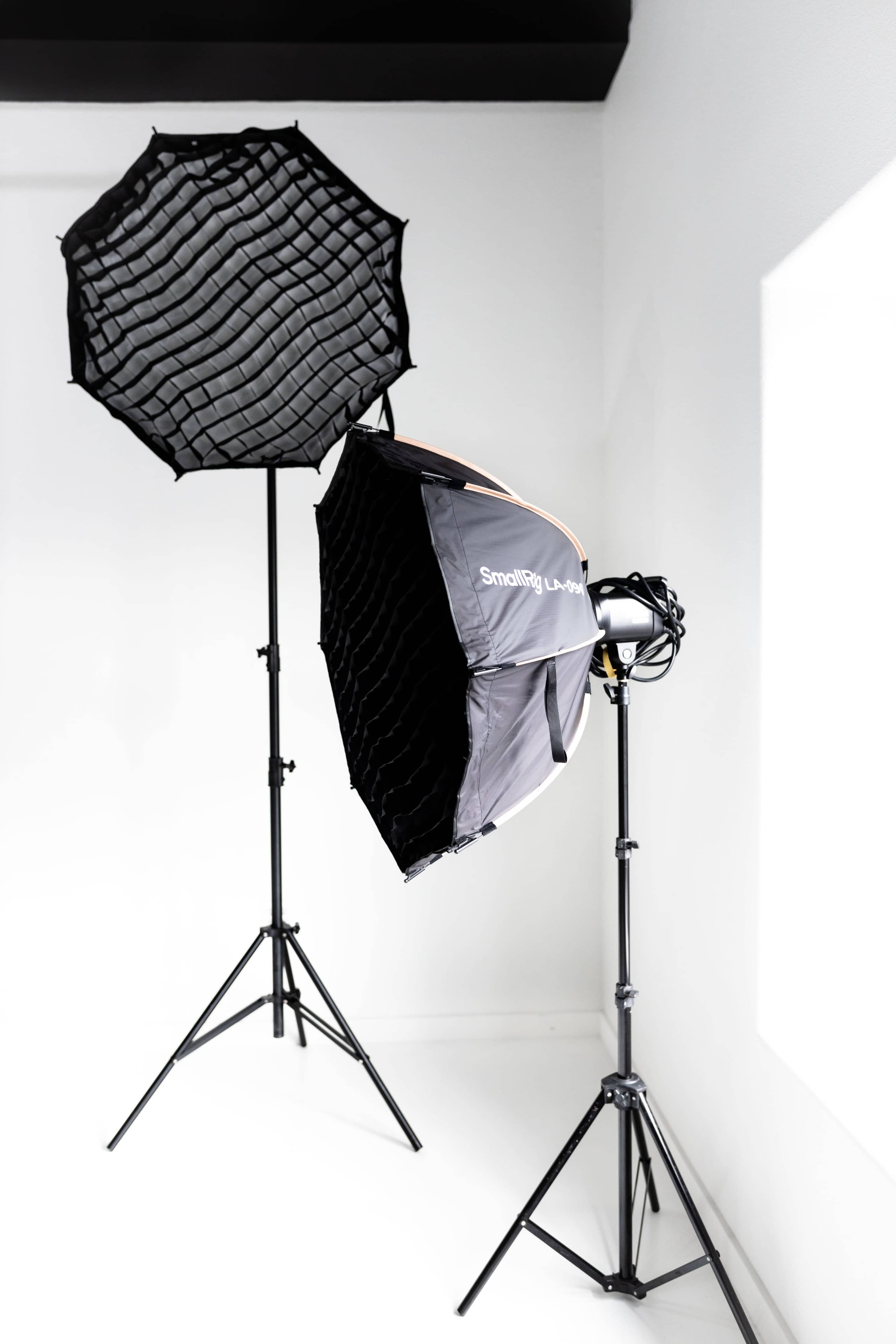 Two photography softboxes are positioned on stands next to a window in a minimalist studio setting.