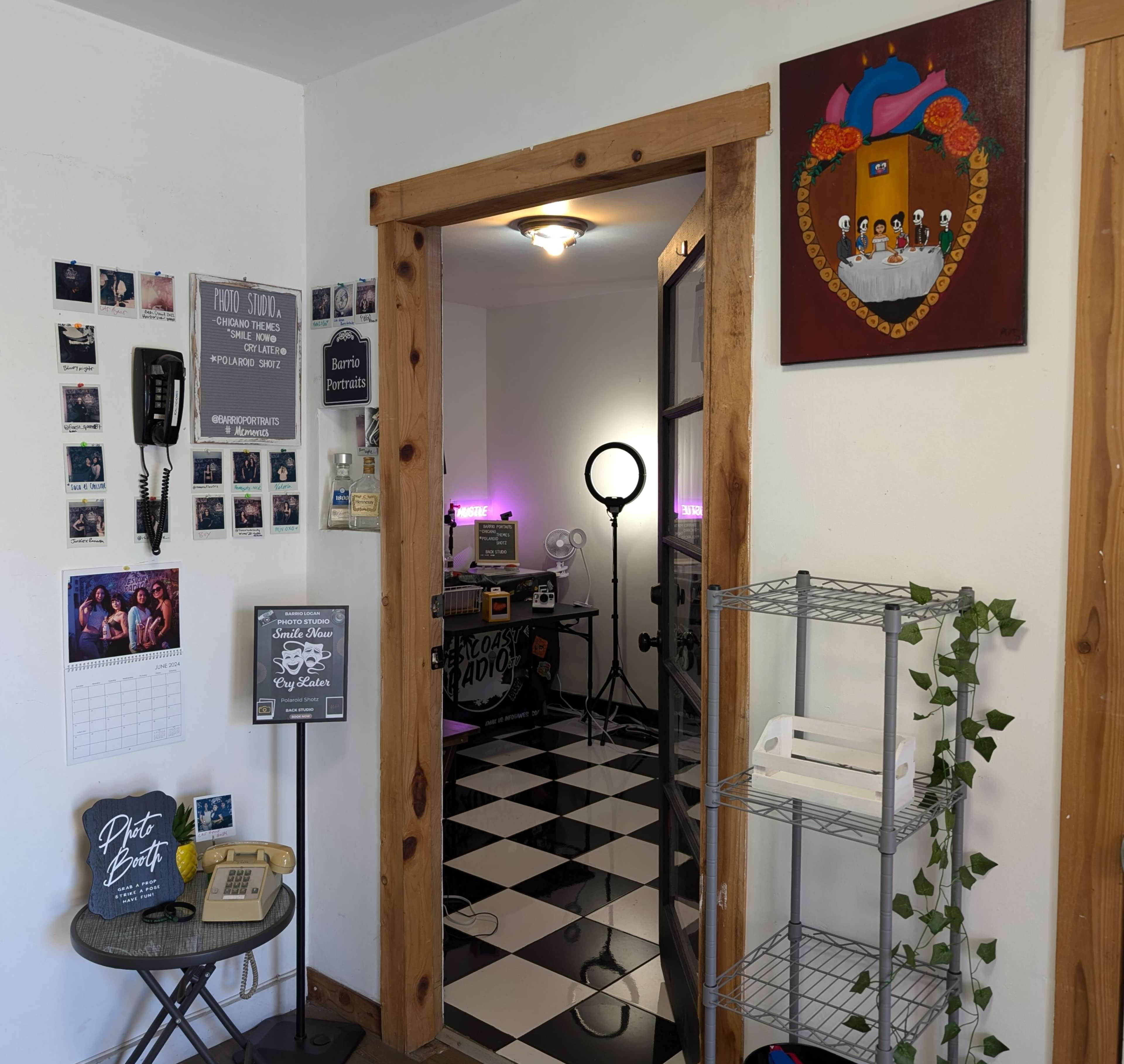 A well-lit room features a doorway leading to a space with checkered flooring, a ring light, and a collection of photographs and art on the walls.