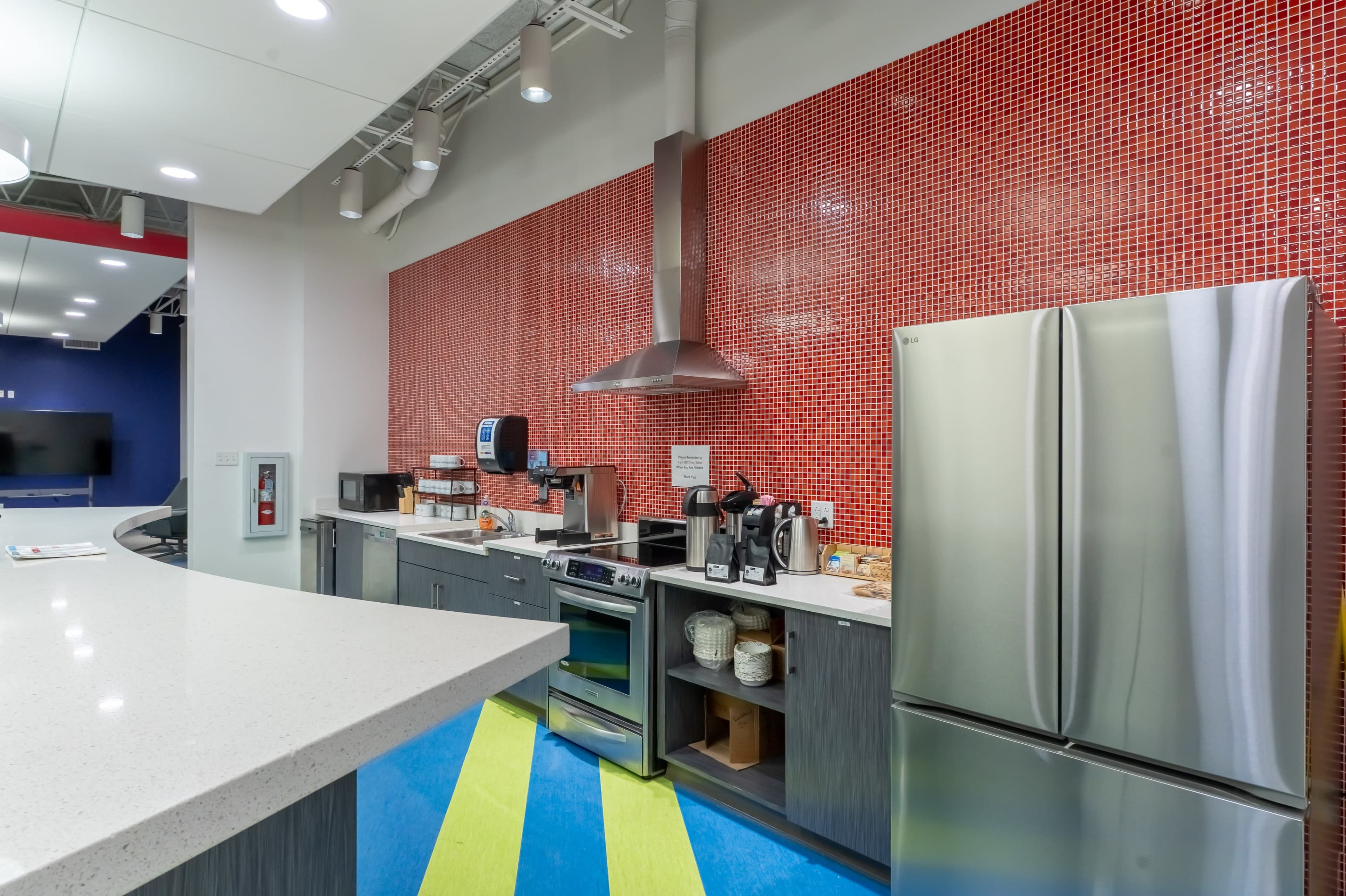 The image shows a modern kitchen area featuring stainless steel appliances, a red mosaic tile backsplash, and a counter with various kitchen utensils and drinks.