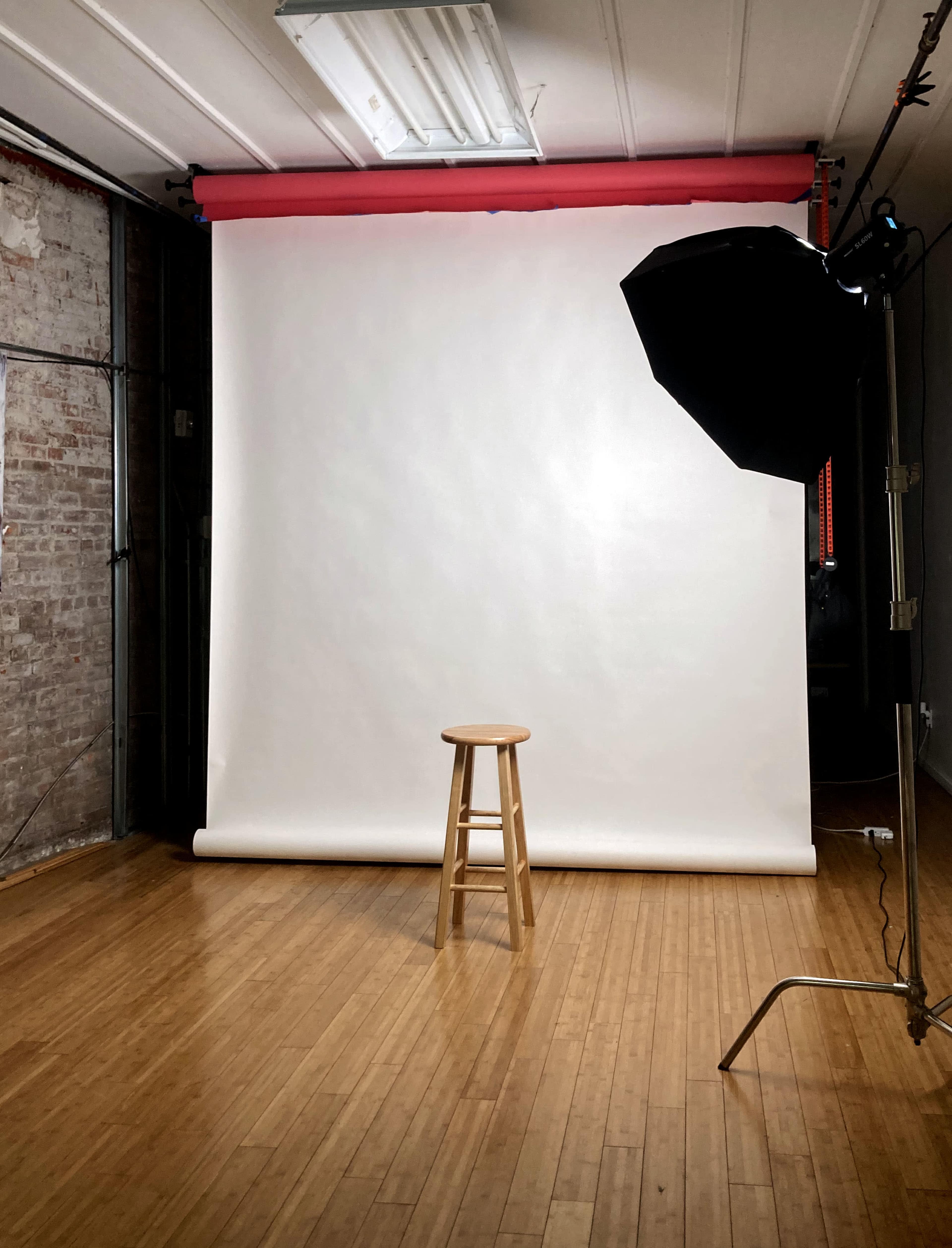A simple photography studio setup with a wooden stool in front of a white backdrop and a light source to the right.