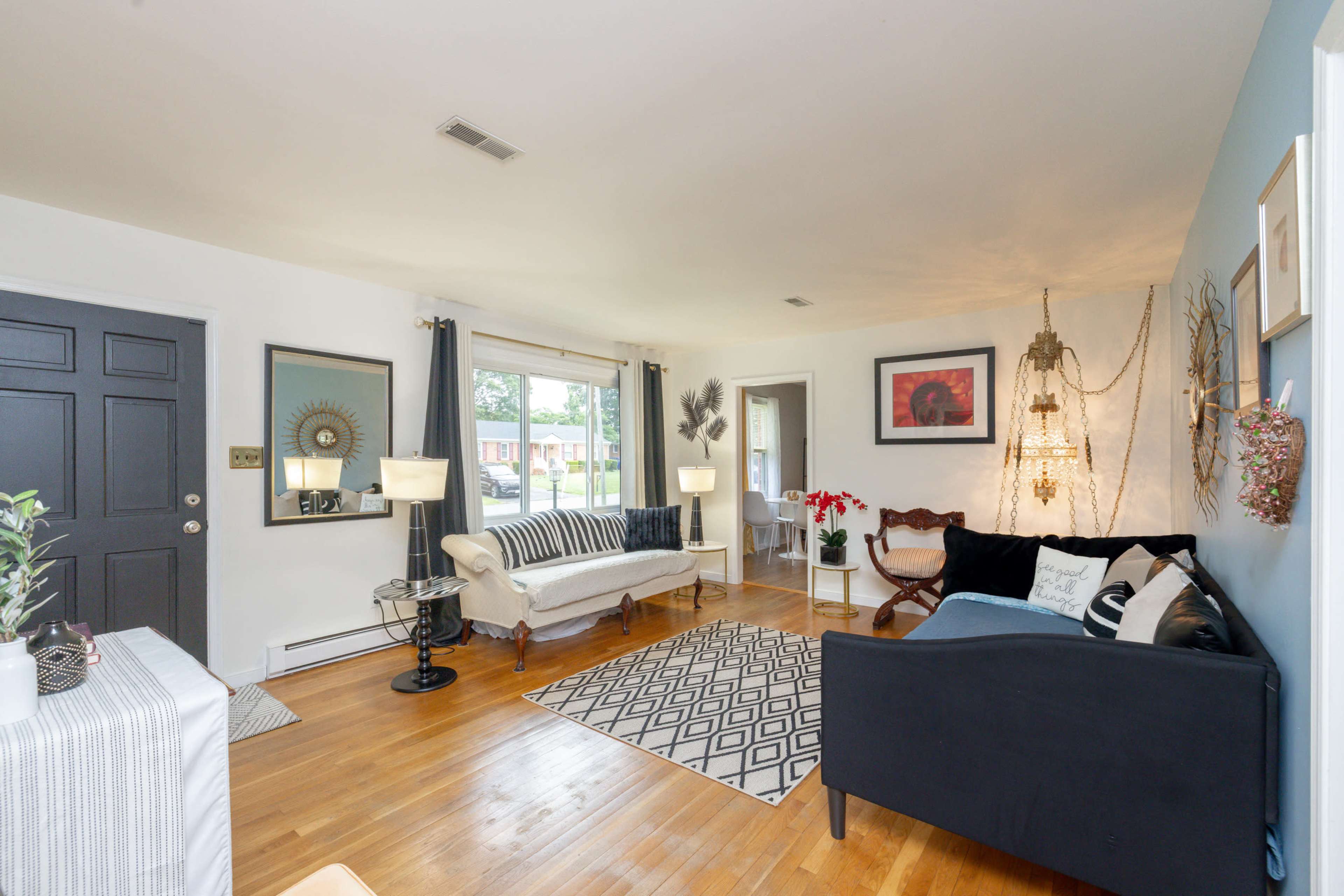 The living room features a mix of seating options, a patterned area rug, and large windows allowing natural light to fill the space.
