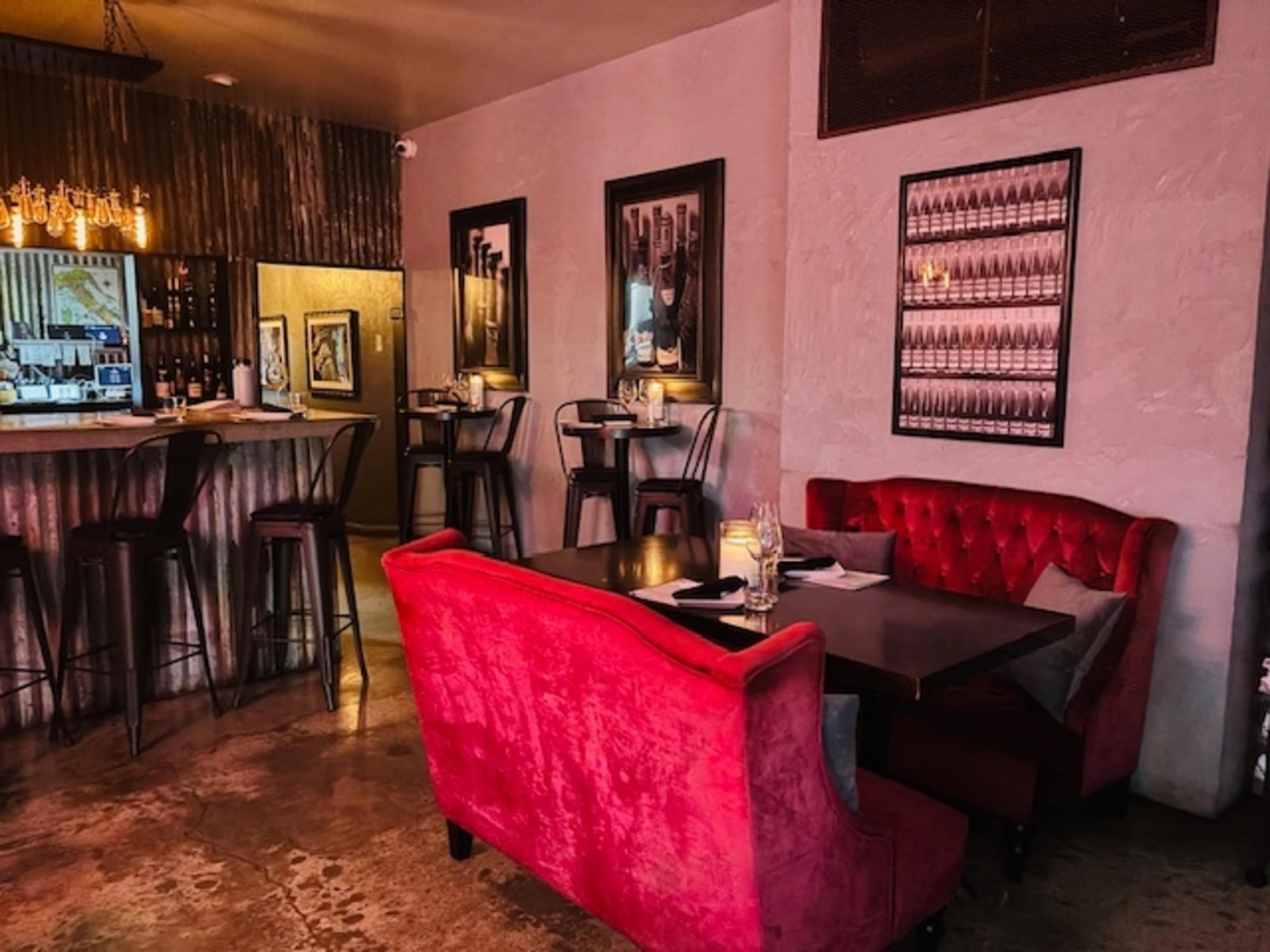 The image shows a stylish restaurant interior featuring a red velvet couch, a wooden table, and an elegant bar area in the background.