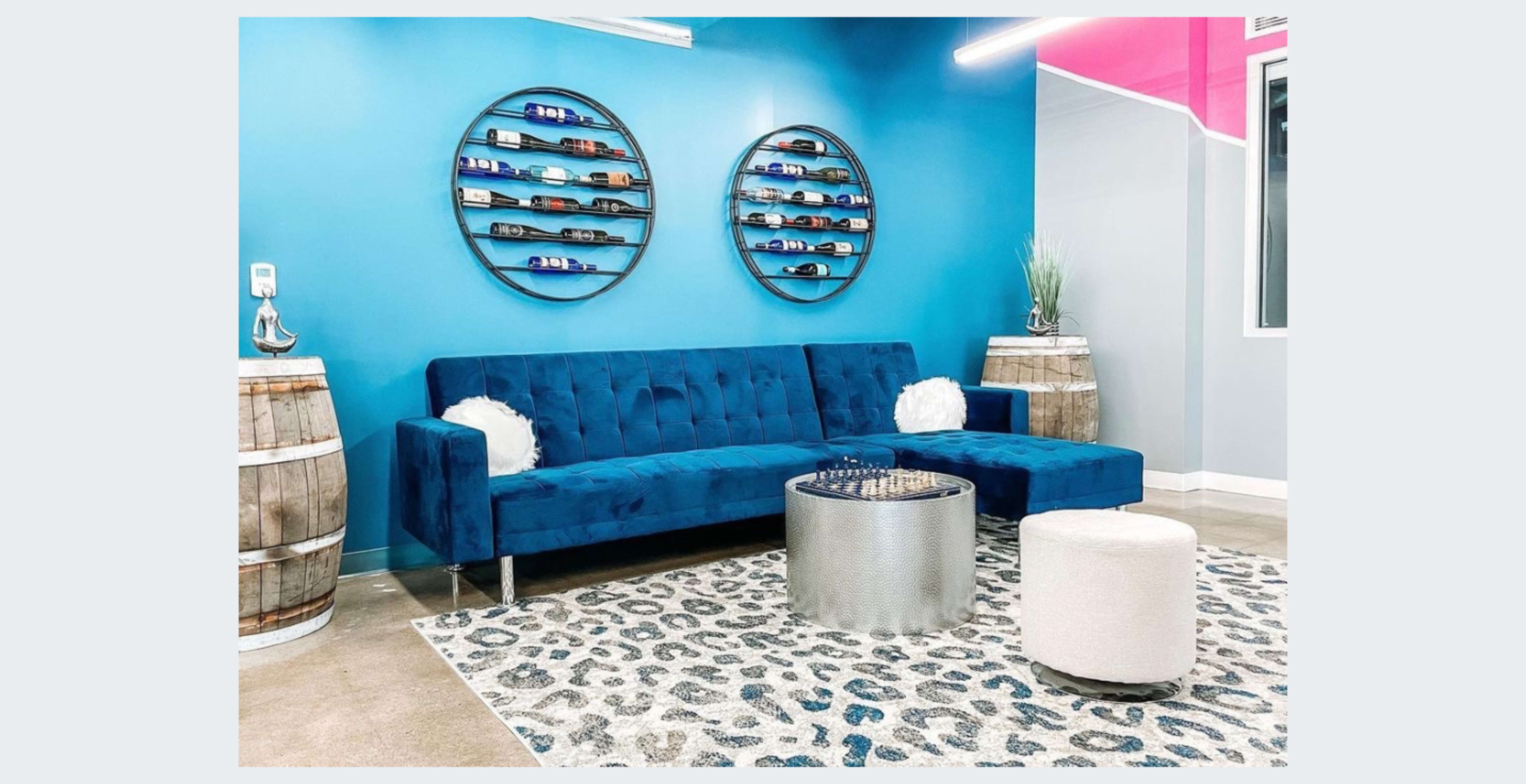 A modern lounge area featuring a blue sofa, round mirrors on the wall, and wooden barrels used as side tables.