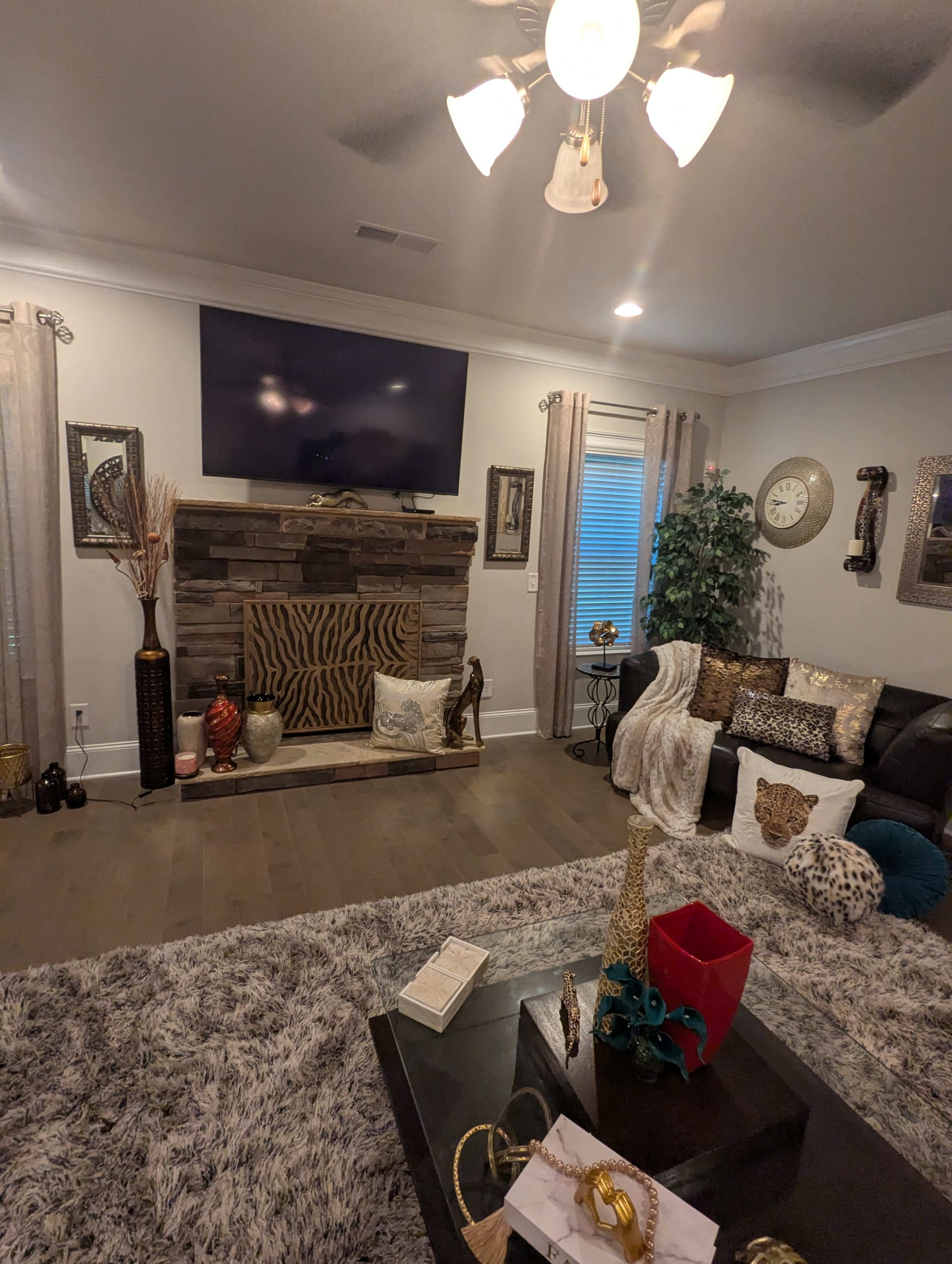 The living room features a large television mounted above a stone fireplace with decorative pillows and animal print accents.