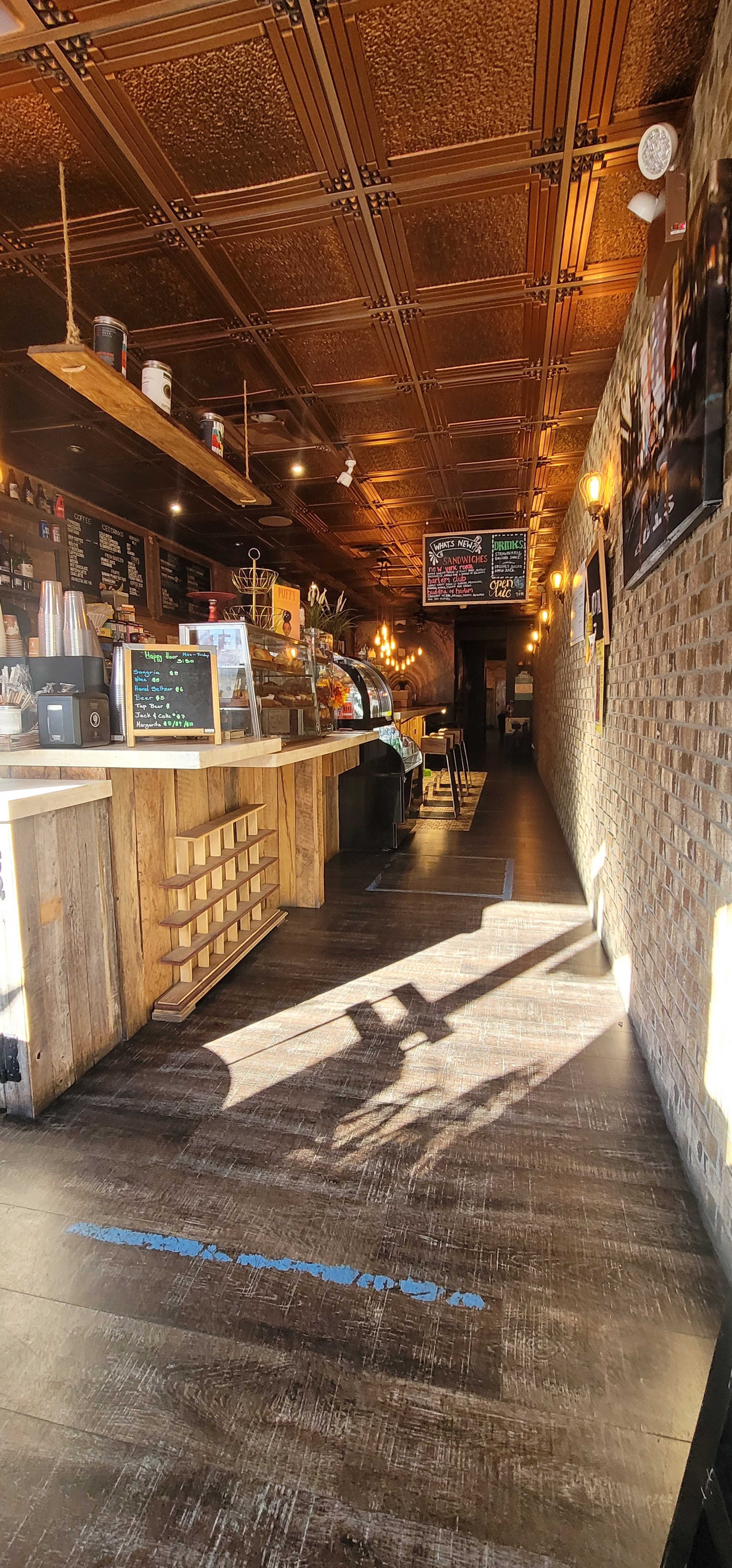The image shows a cozy café interior with wooden counters, exposed brick walls, and a long corridor leading to a darkened area in the background.
