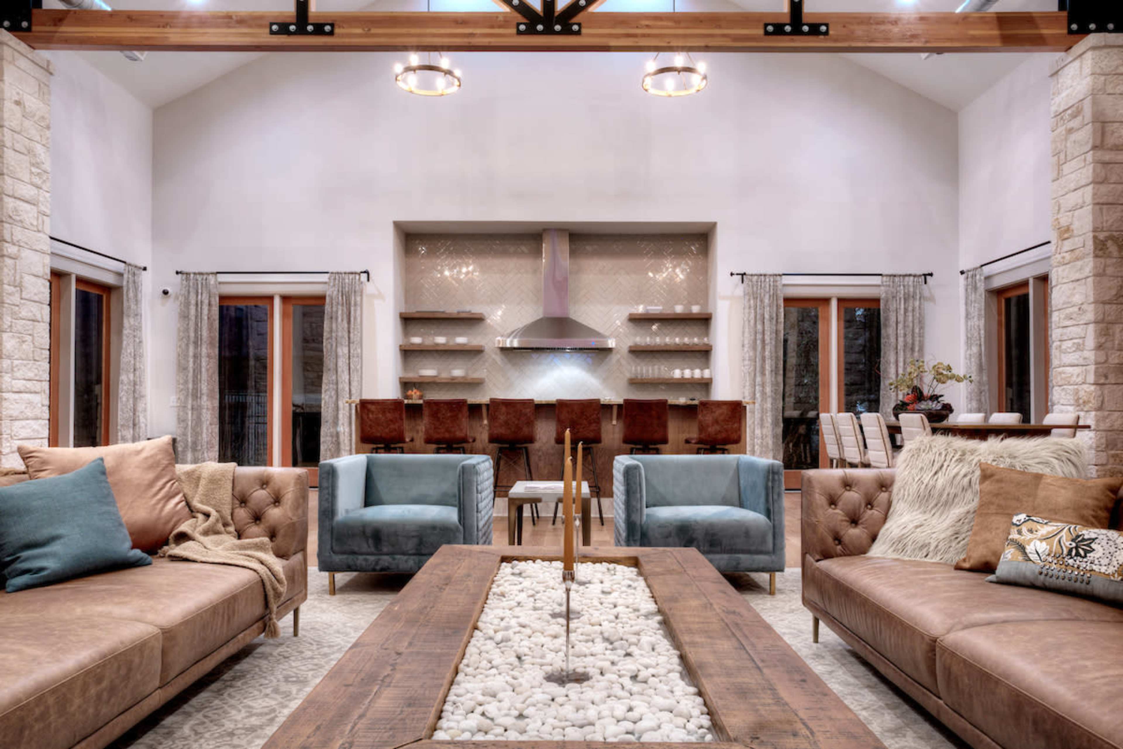 A modern living room with two sofas, a coffee table containing pebbles, and a kitchen area in the background.