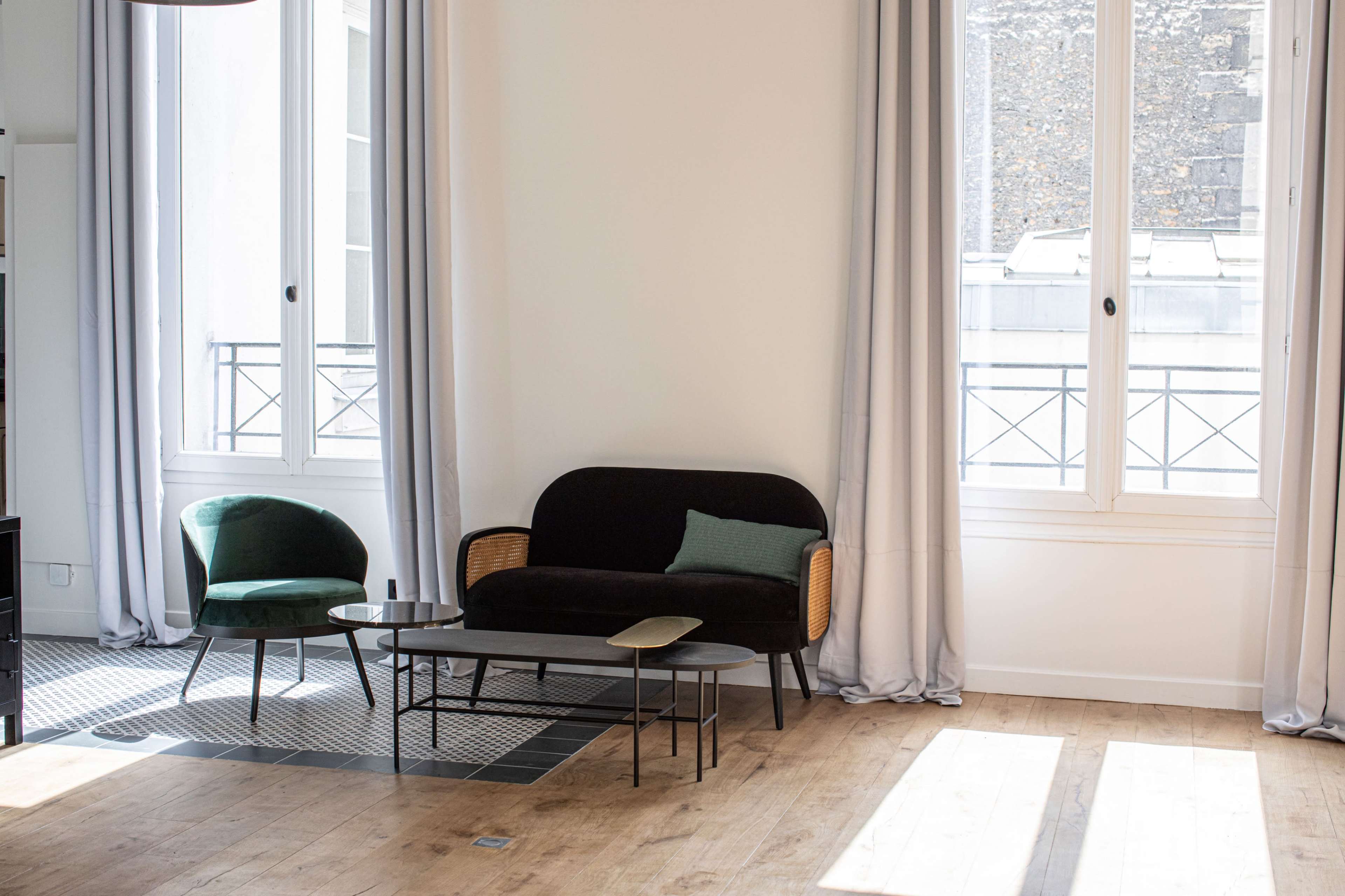 A minimalist living room with a black sofa, two armchairs, and a coffee table near large windows.