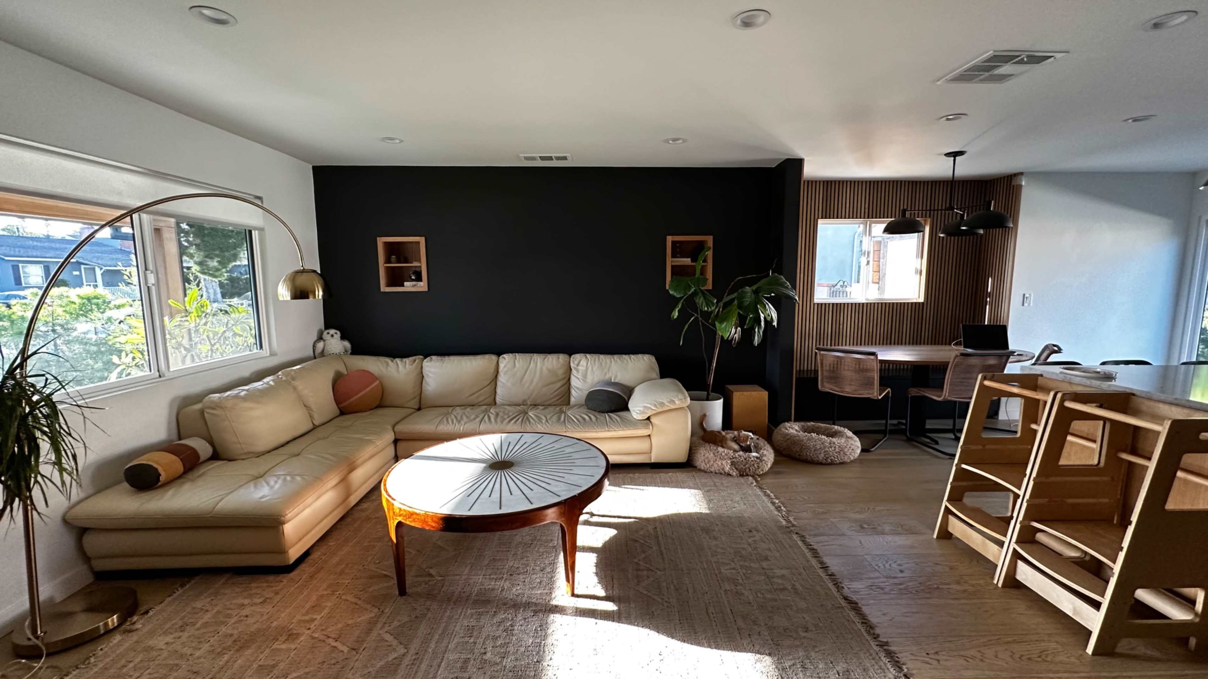 A bright, modern living space featuring a light-colored sectional sofa, a round coffee table, and a dining area with wooden chairs and a table.