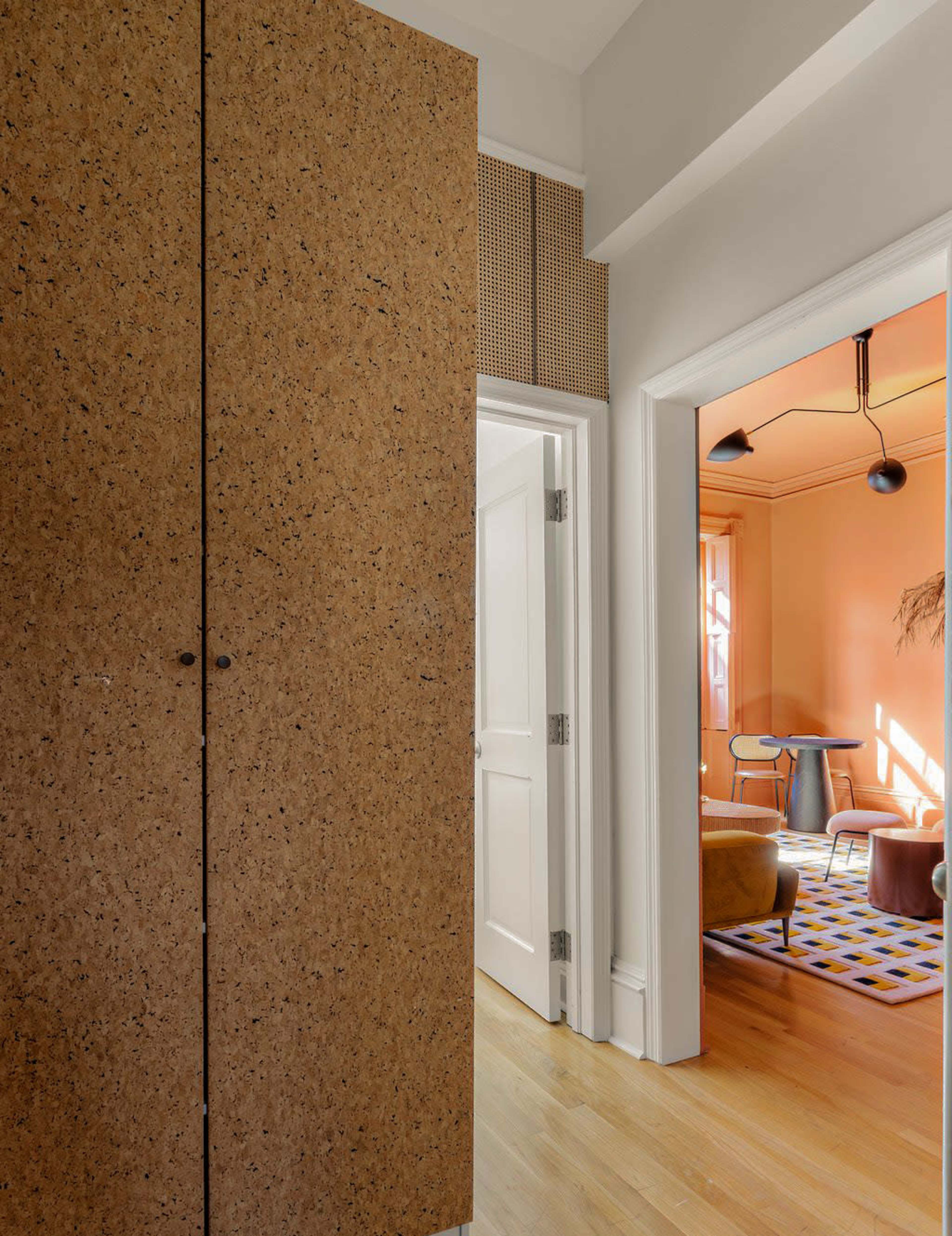 A hallway with a cork-textured cabinet and an open doorway leading to a brightly lit room featuring a table and chairs.