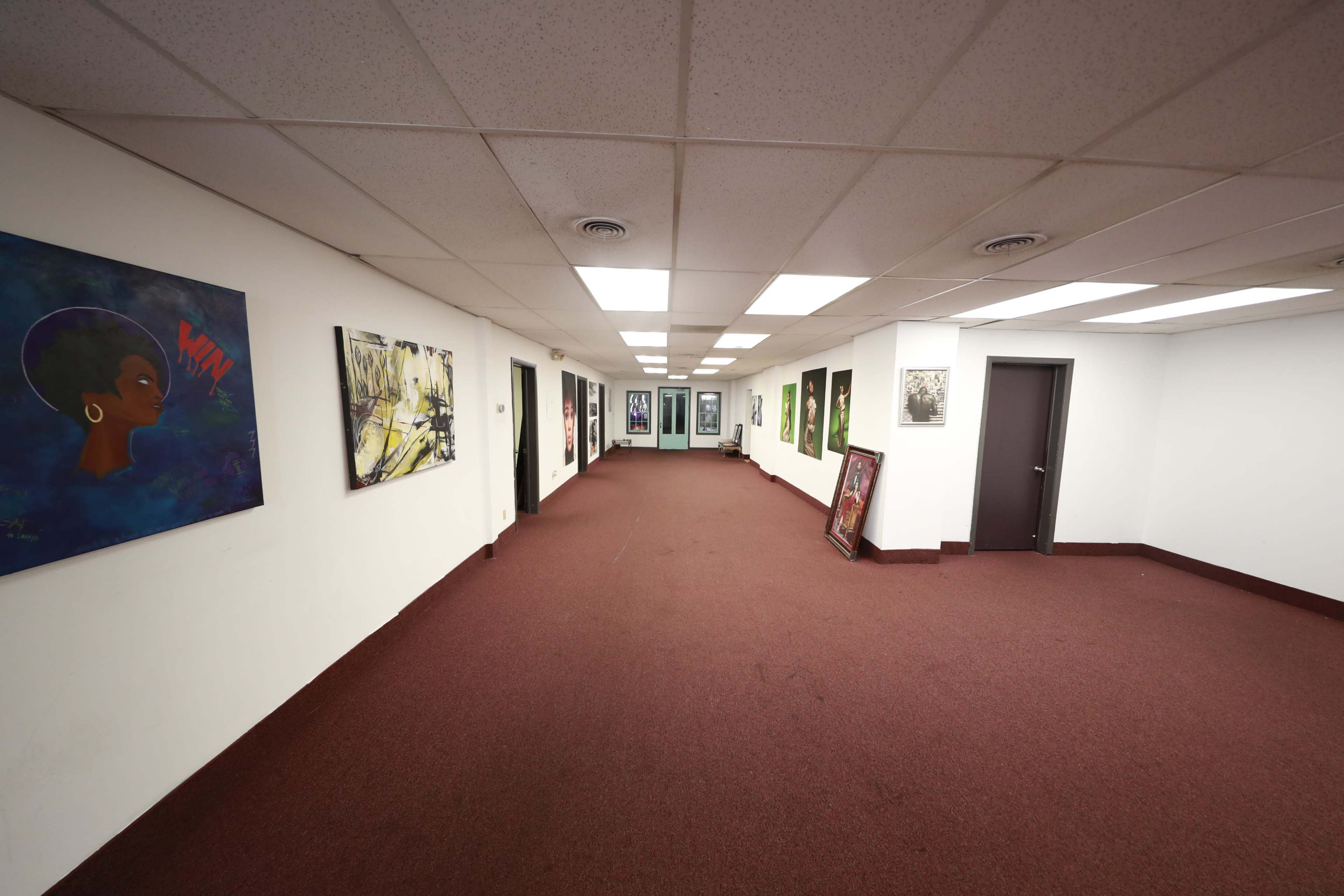 A long hallway with artwork on the walls and a carpeted floor, leading to a set of glass doors at the far end.