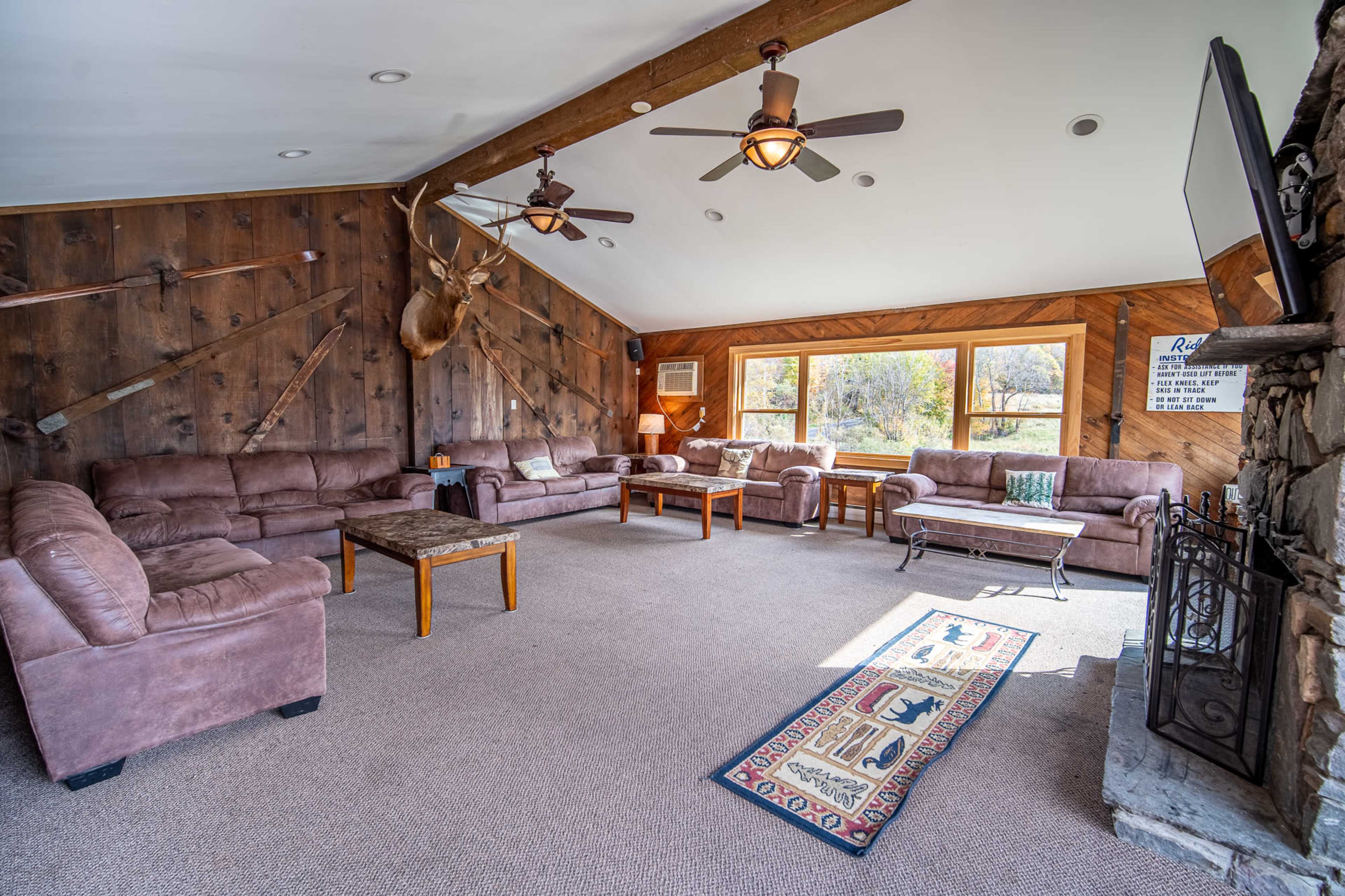 A cozy living room featuring brown sofas arranged around a wooden coffee table, with a stone fireplace and a large window displaying a view of the outdoors.