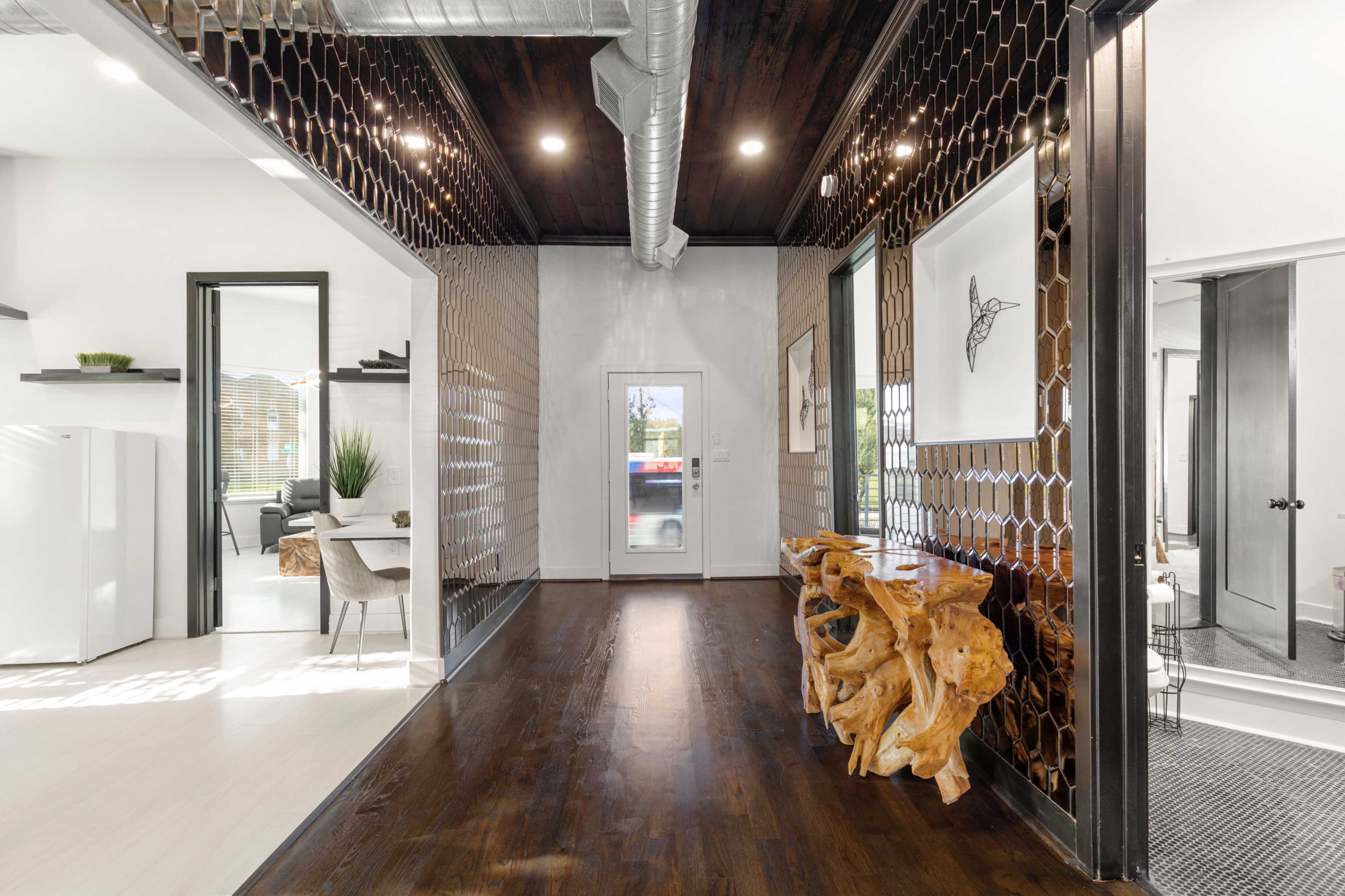 A modern hallway featuring a natural wood console table, hexagonal patterned wall, and large windows leading to an outdoor area.