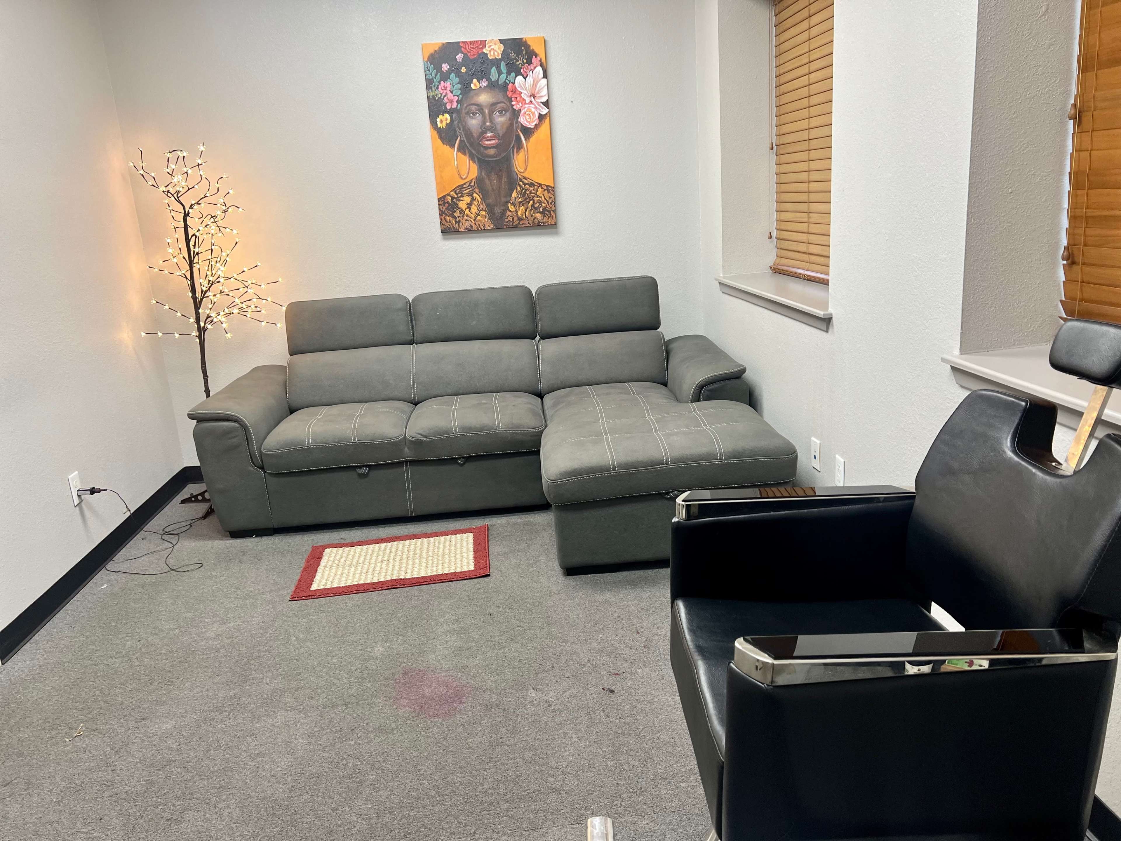 A gray sectional sofa and a black salon chair in a room with a lighted decorative tree and a colorful artwork on the wall.