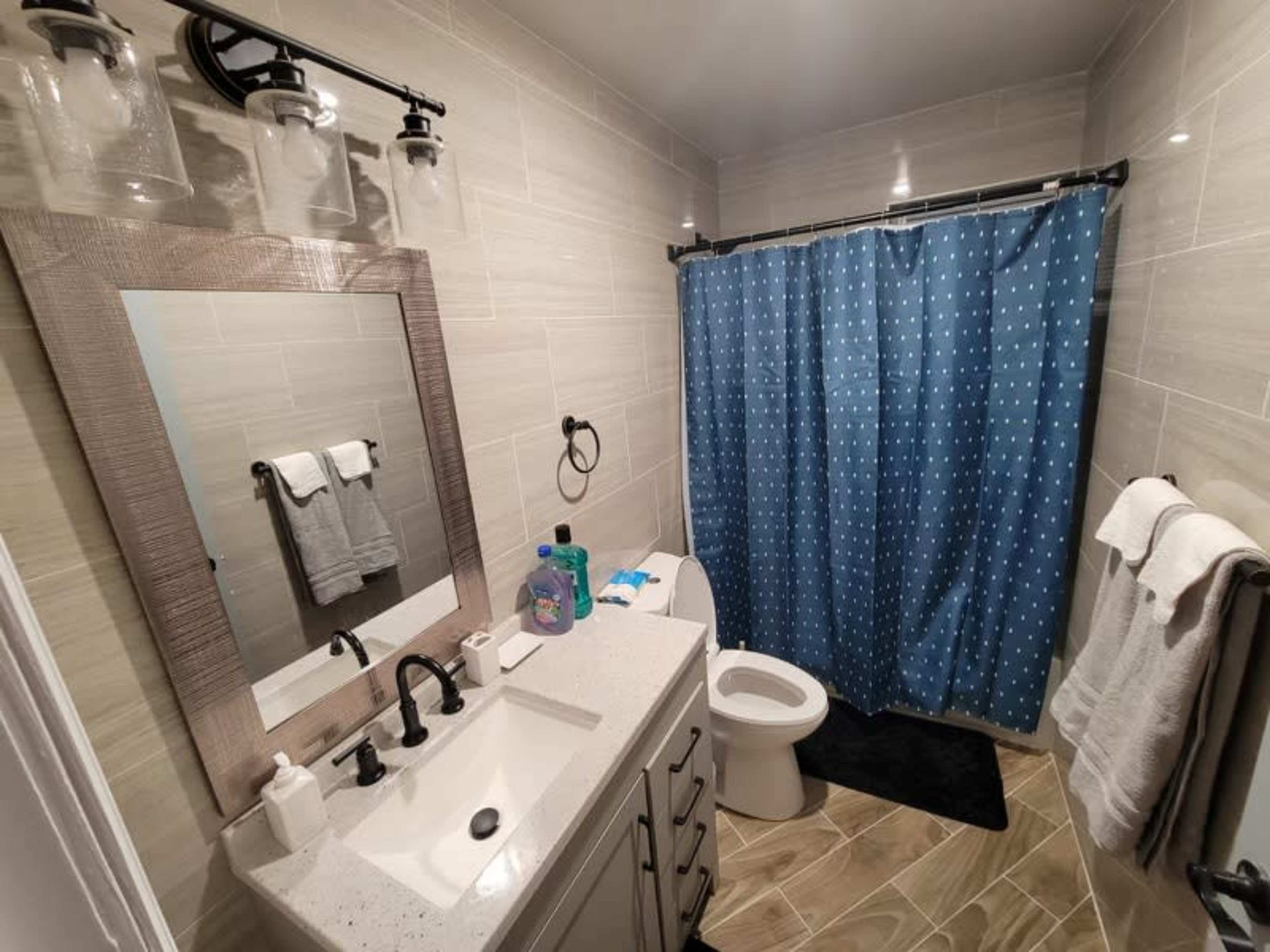The image shows a bathroom with a vanity, a mirror, a shower curtain with blue polka dots, and a toilet.