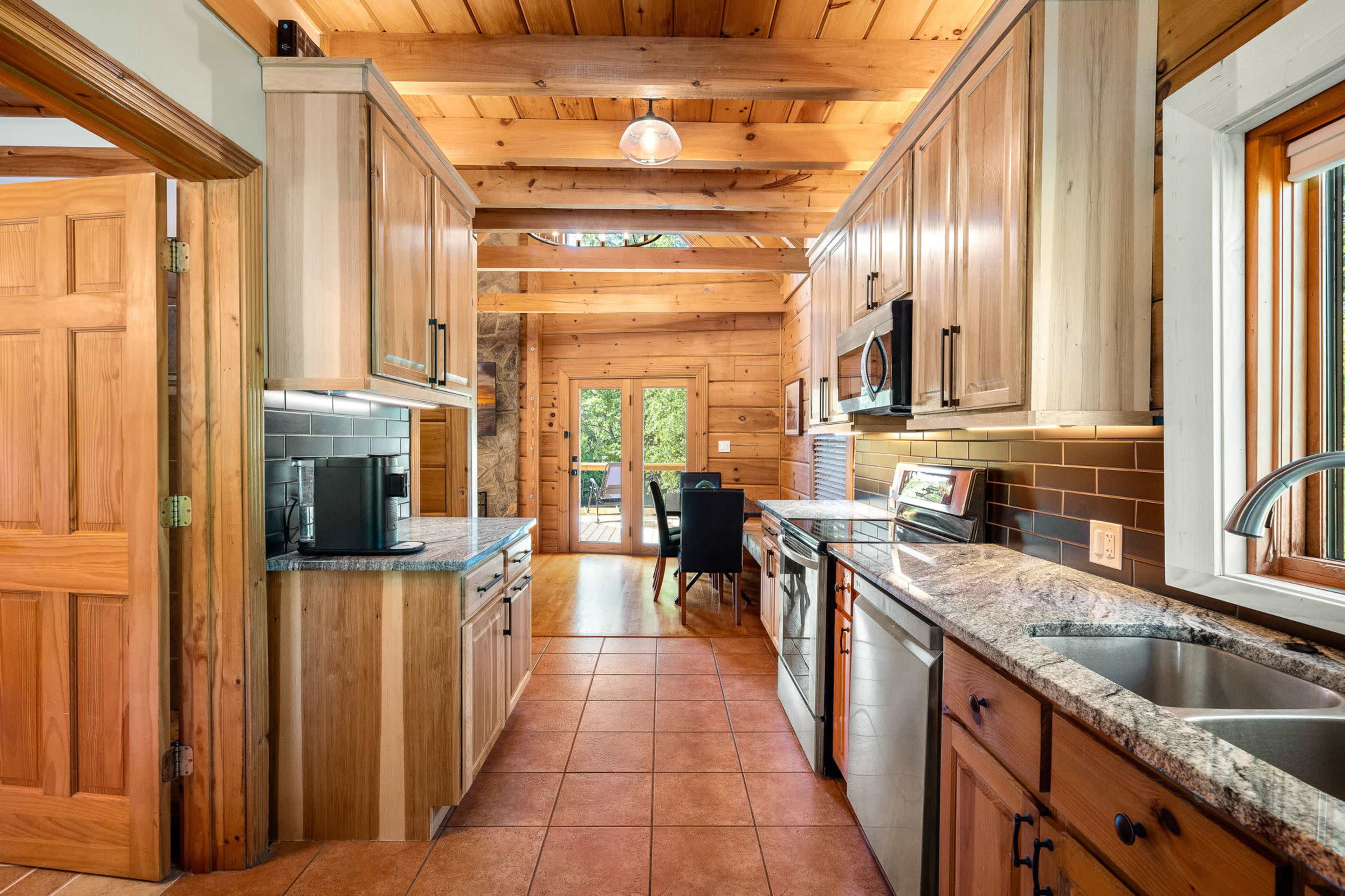A rustic kitchen with wooden cabinets, granite countertops, and a view of a patio through a large window.