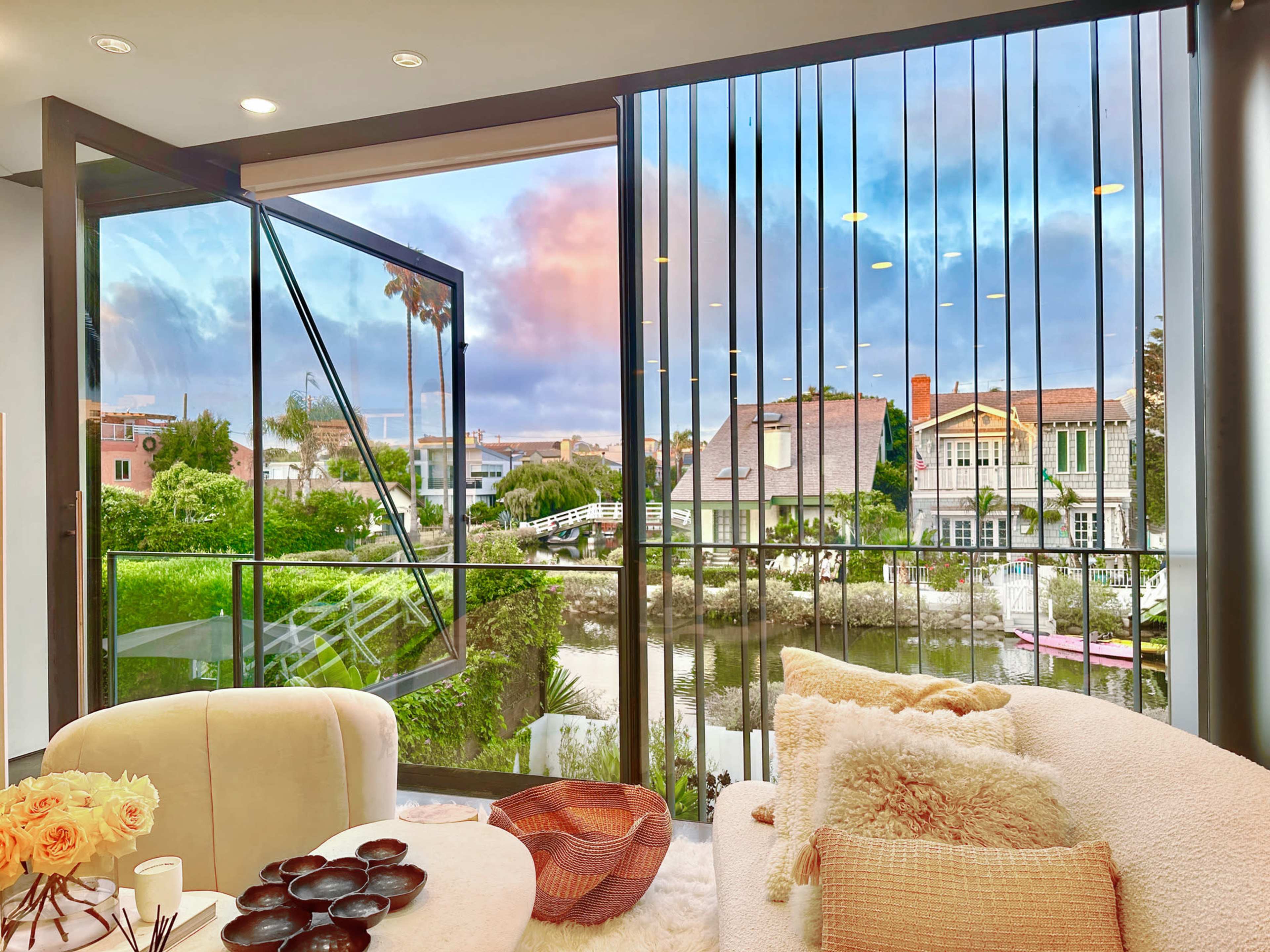 A modern living room features an open window overlooking a scenic canal and residential area with greenery.
