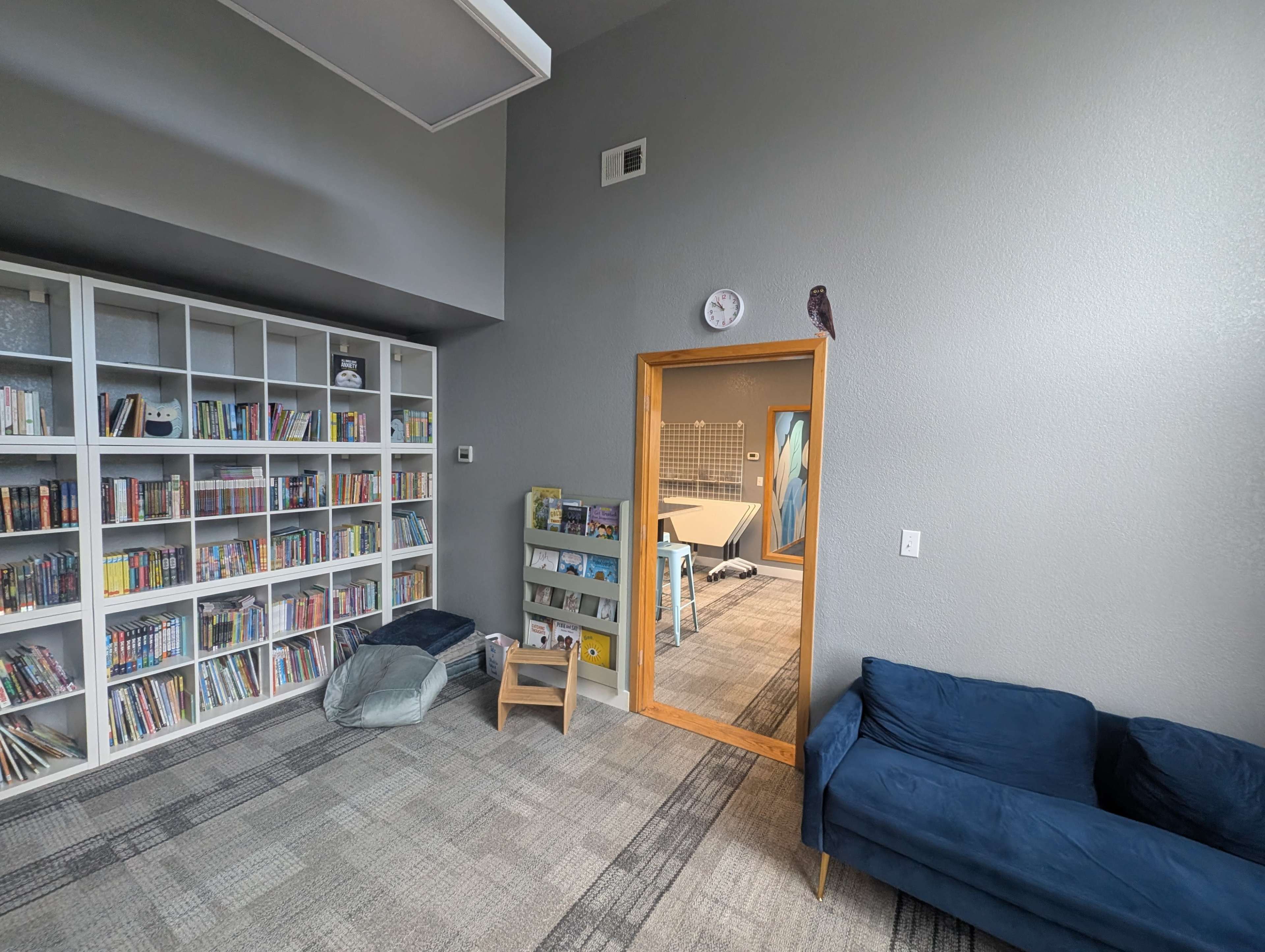 The image shows a cozy room with shelves filled with books, a small couch, and a door leading to another space.
