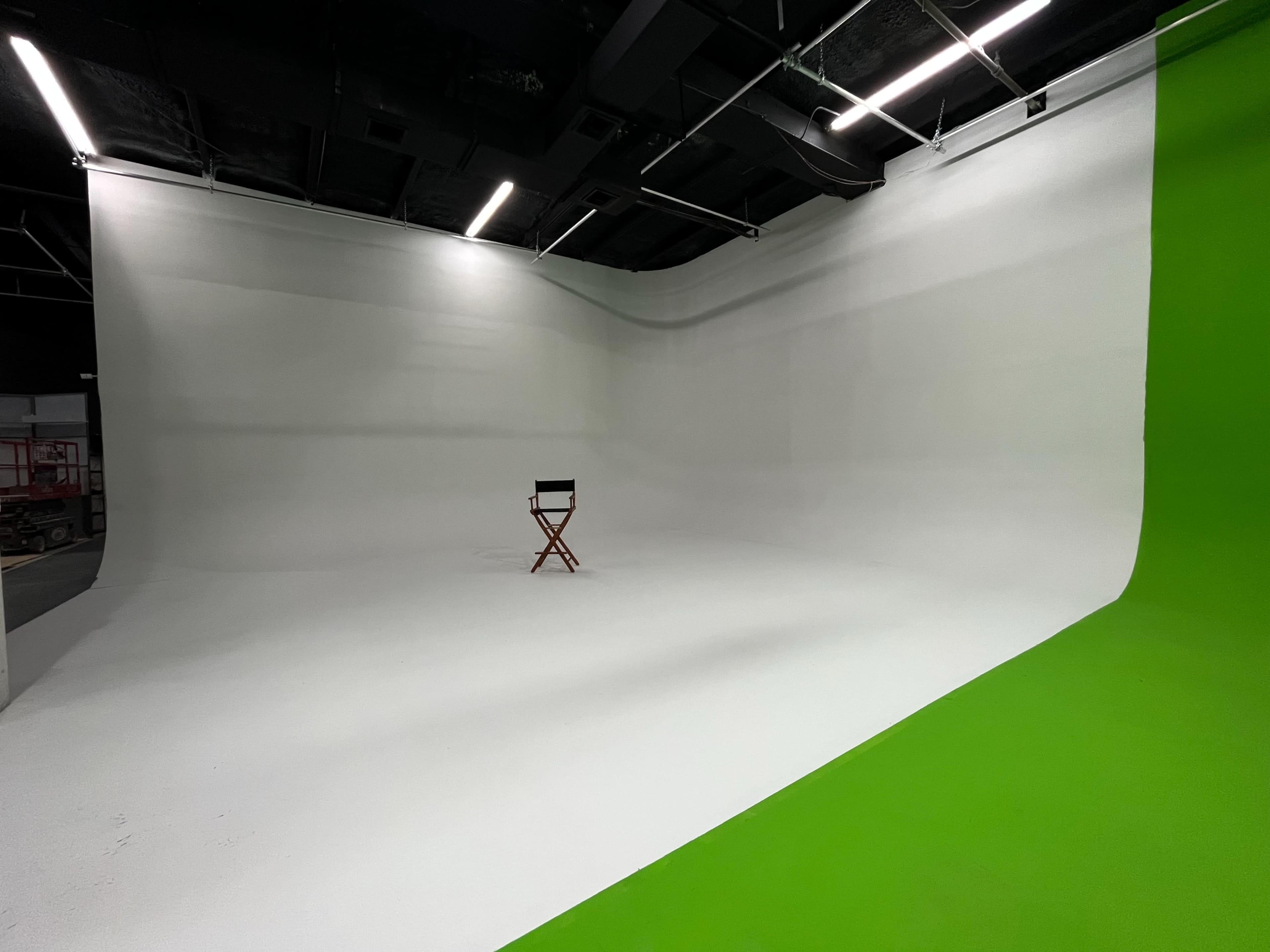 The image shows a spacious studio with a white backdrop and a green side wall, featuring a single director's chair in the center.