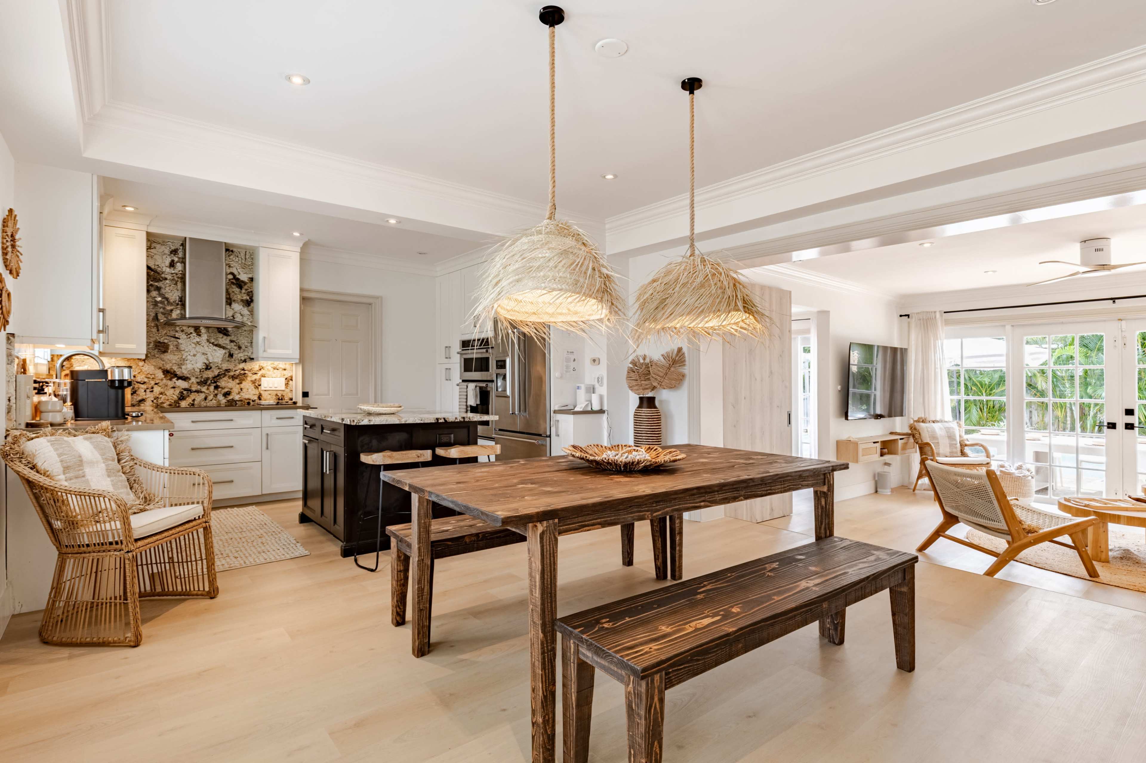 The image shows a modern kitchen and dining area with a wooden table, straw pendant lights, and a mix of seating options, including woven chairs and a sofa.