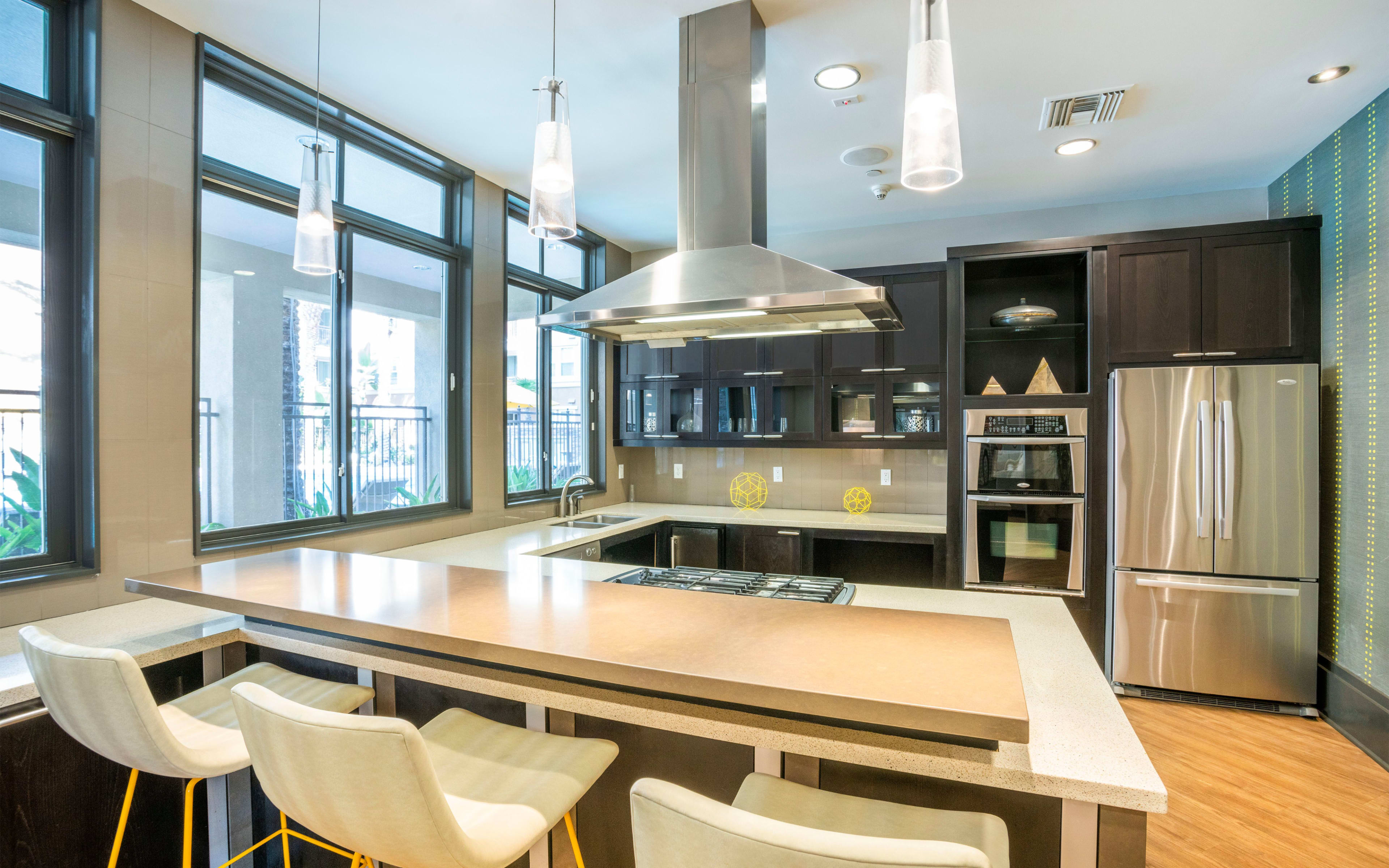 A modern kitchen features a central island with seating, stainless steel appliances, and large windows that provide natural light.