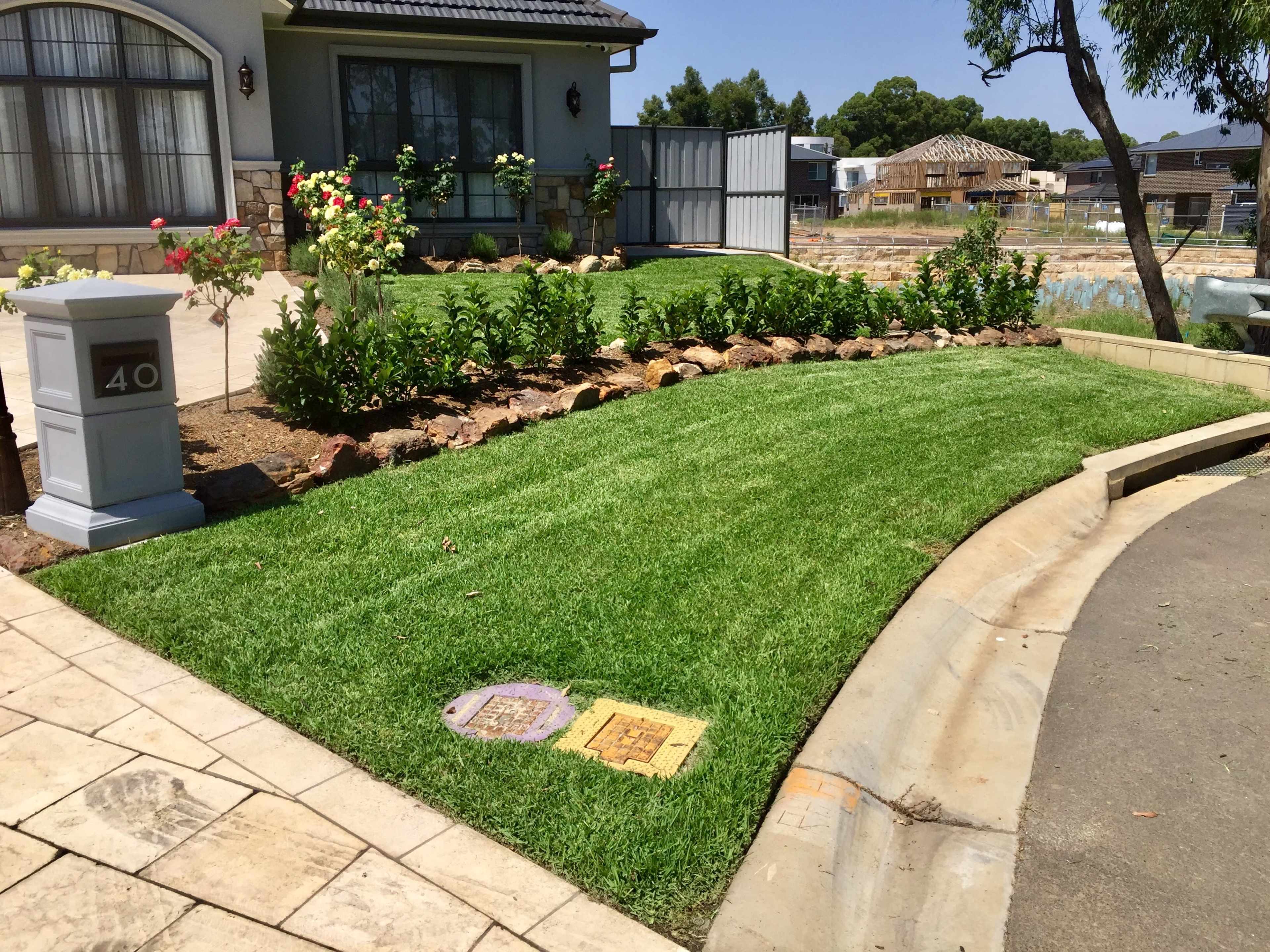 A well-manicured front yard with a neatly edged lawn, bordered by flower beds and a stone pathway in front of a house.