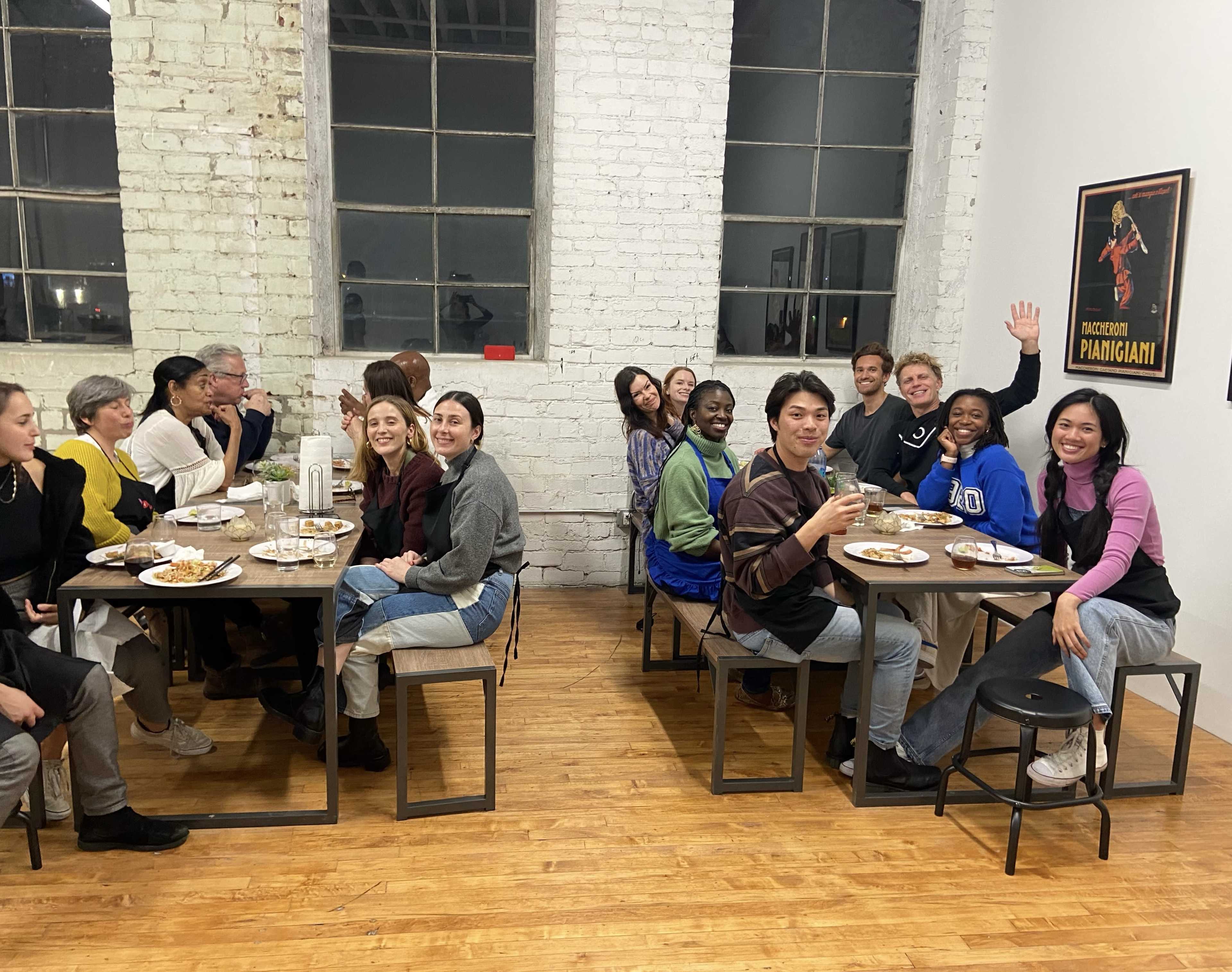 A group of people is seated at tables sharing a meal in a brightly lit room with large windows.
