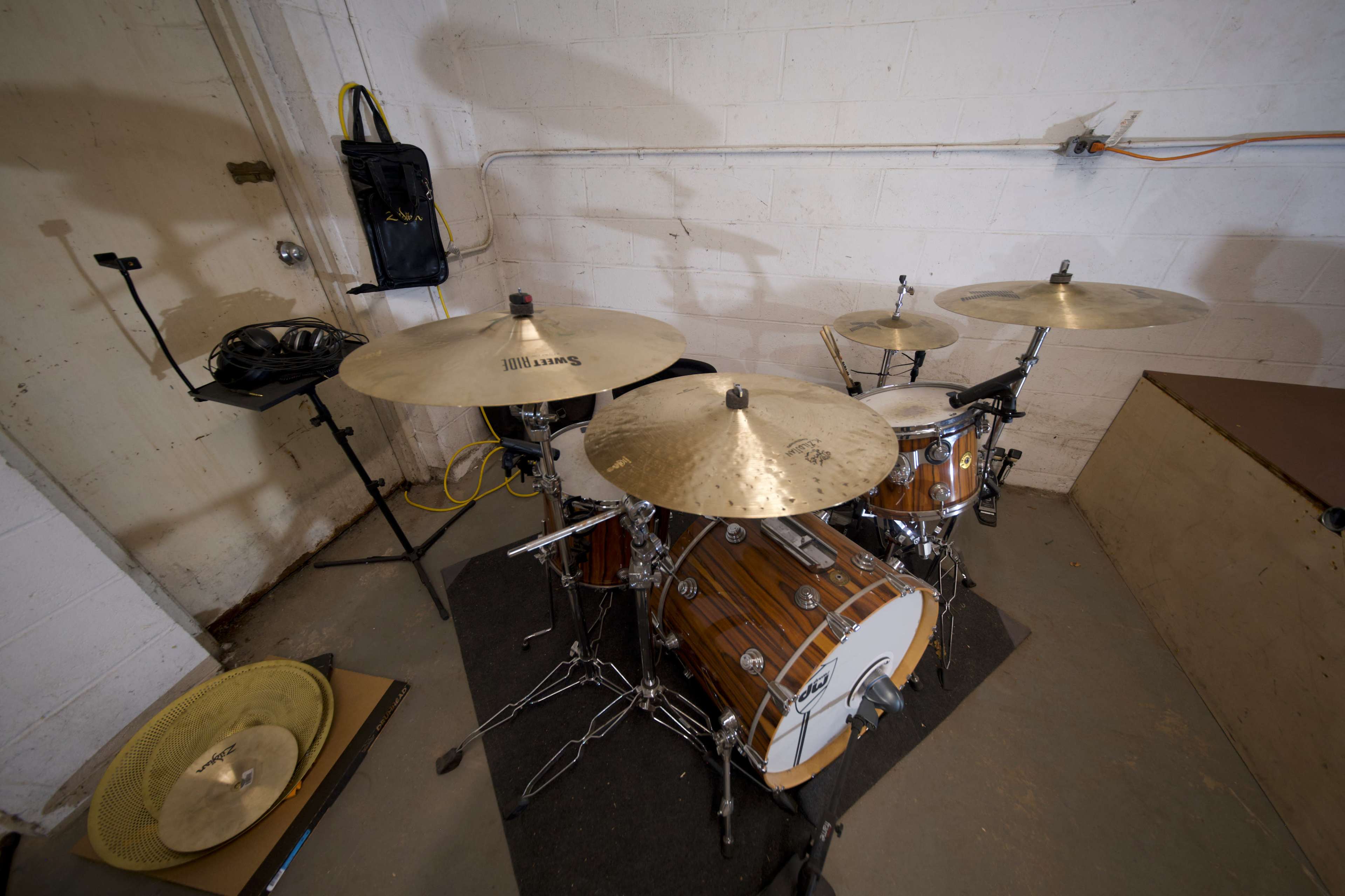 A drum set with wooden accents positioned on a carpeted surface in a room with concrete walls.