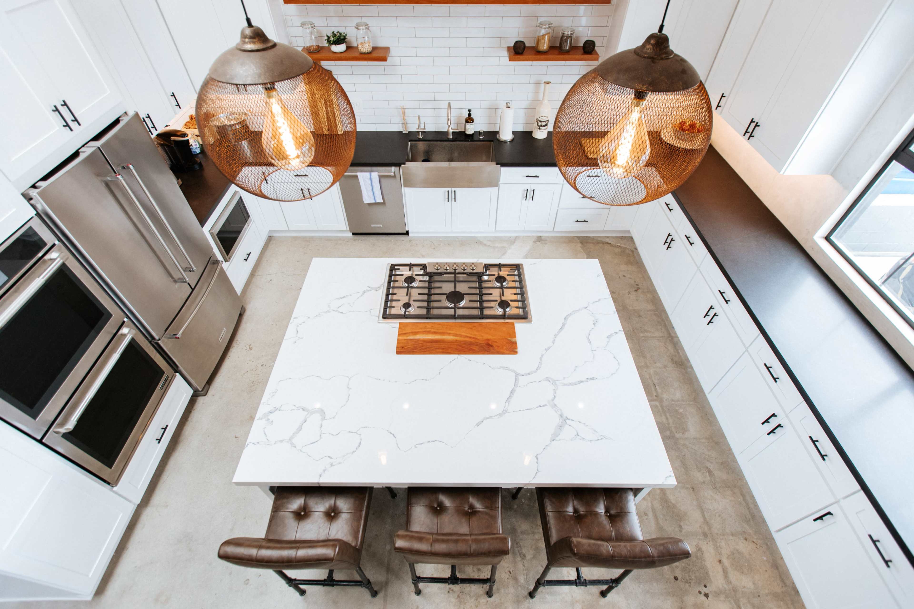 A modern kitchen with white cabinetry, a large marble island with seating, and pendant lights above.