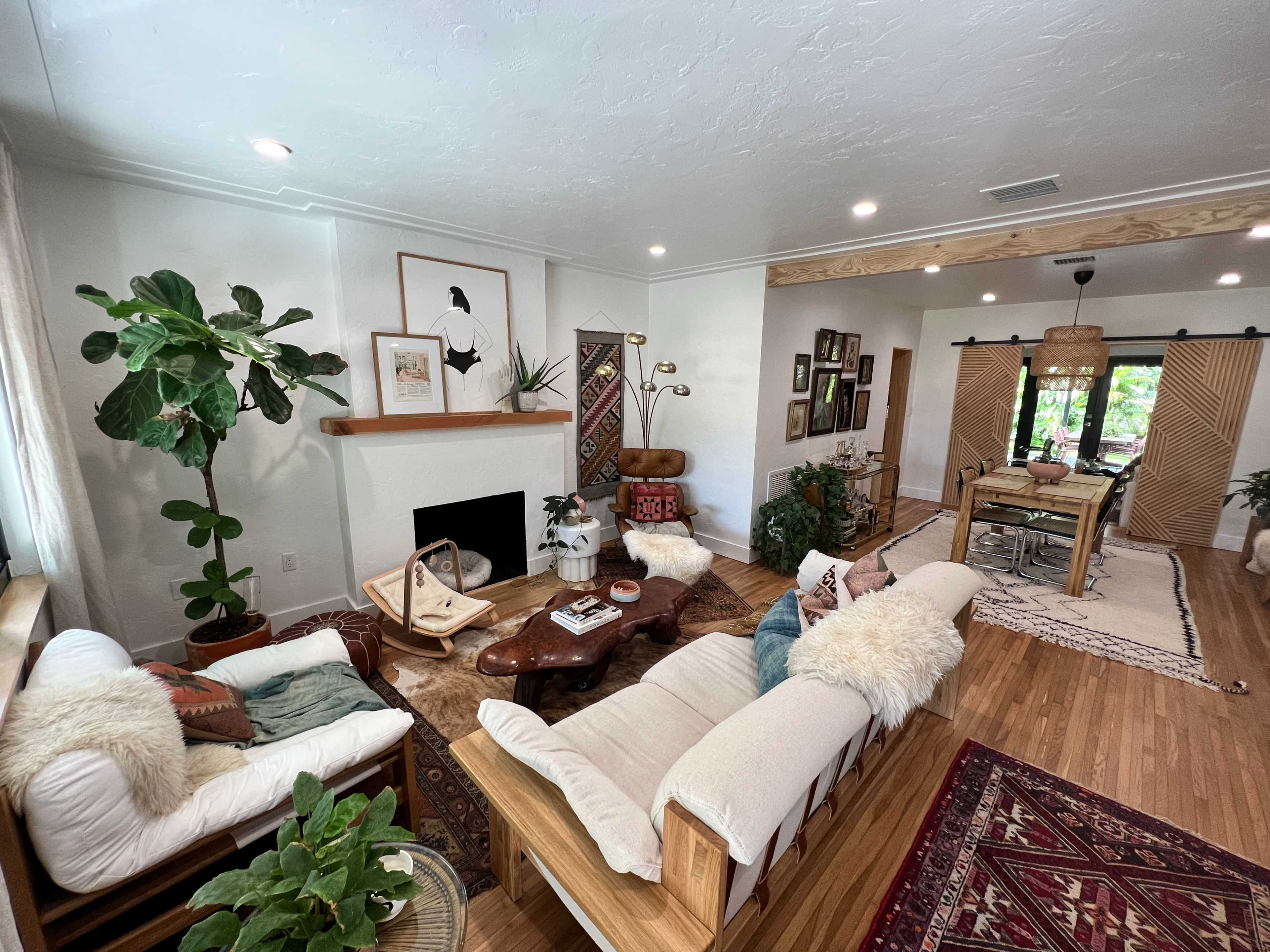 A cozy living room with two sofas, a coffee table, plants, and a dining area in the background.