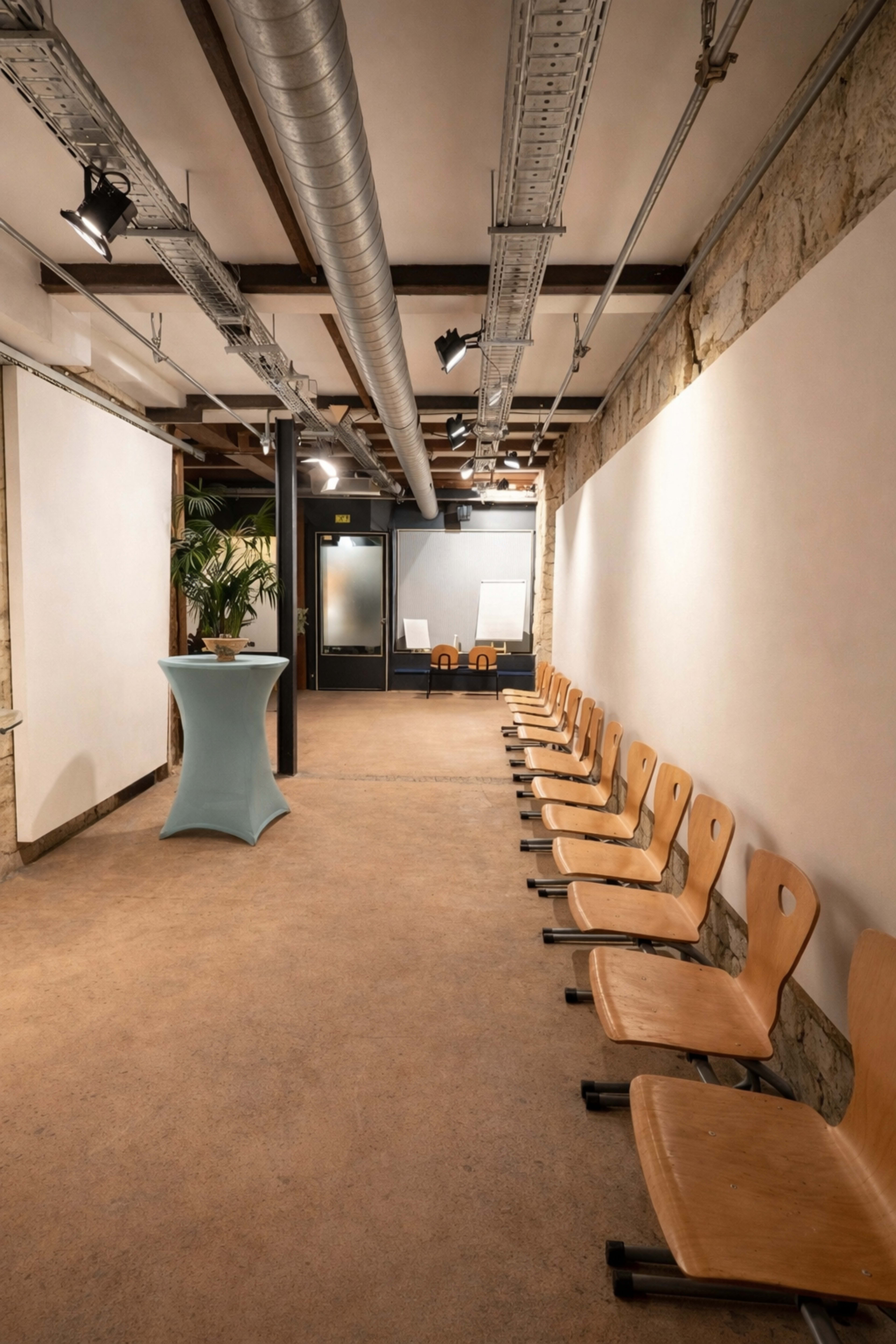 A corridor features a row of wooden chairs along one wall and a podium near the center, leading to a glass-paneled room at the end.