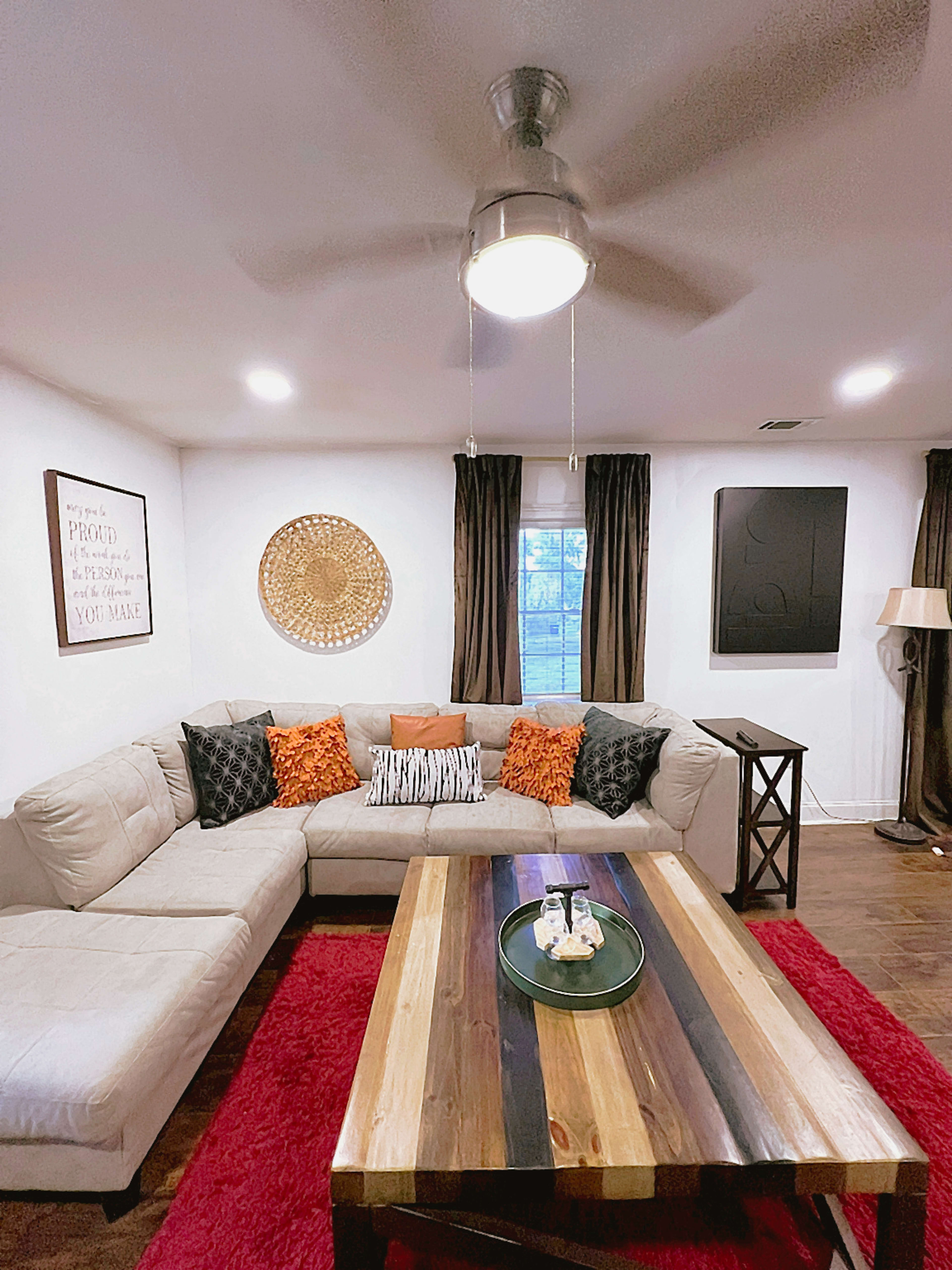 The living room features a sectional couch with decorative pillows, a wooden coffee table, a rug, and artwork on the walls.