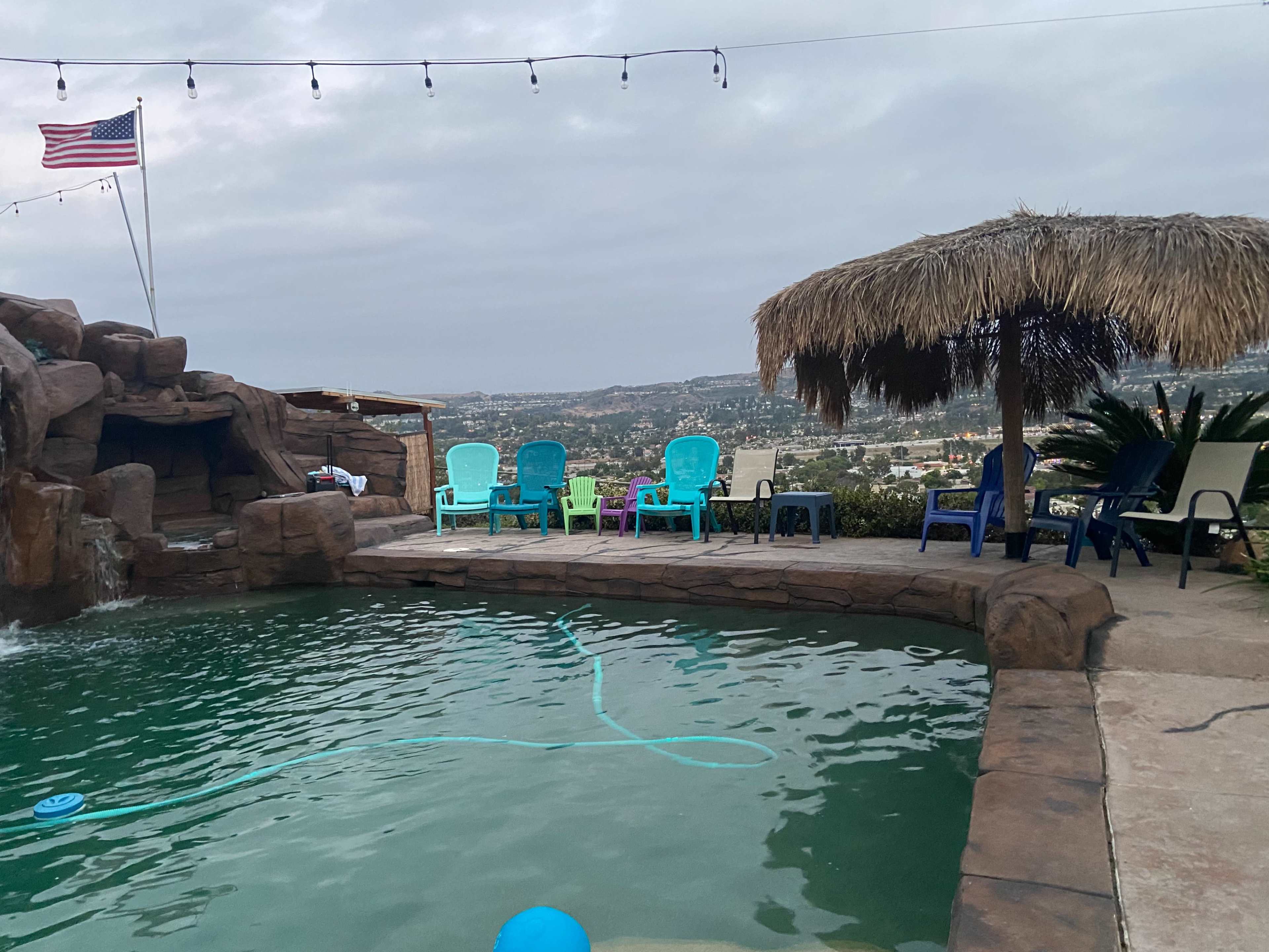 A pool area with colorful chairs and a thatched-roof cabana, overlooking a scenic view.