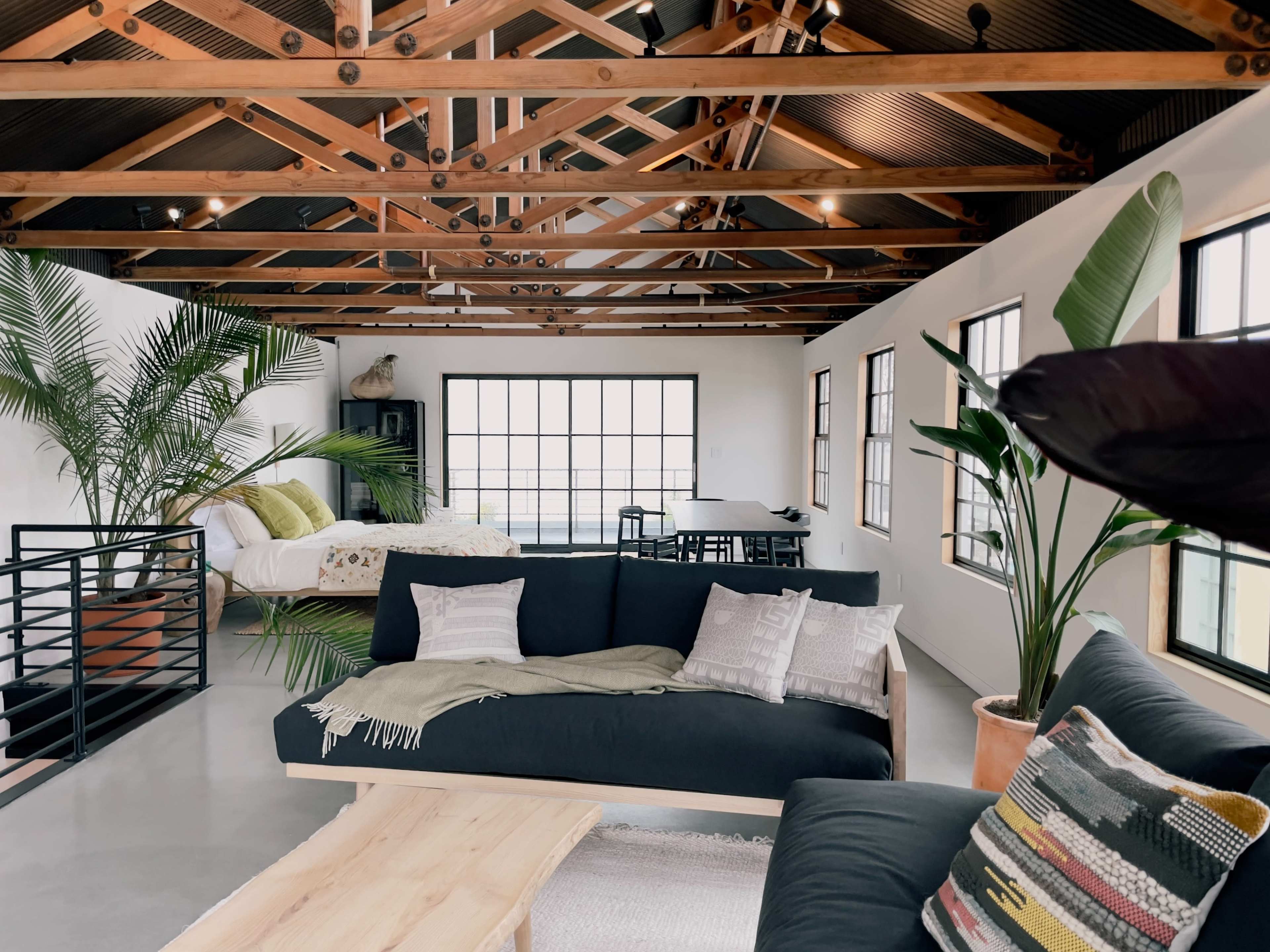 A spacious interior with a modern living area featuring a dark sofa, wooden accents, and large windows allowing ample natural light.