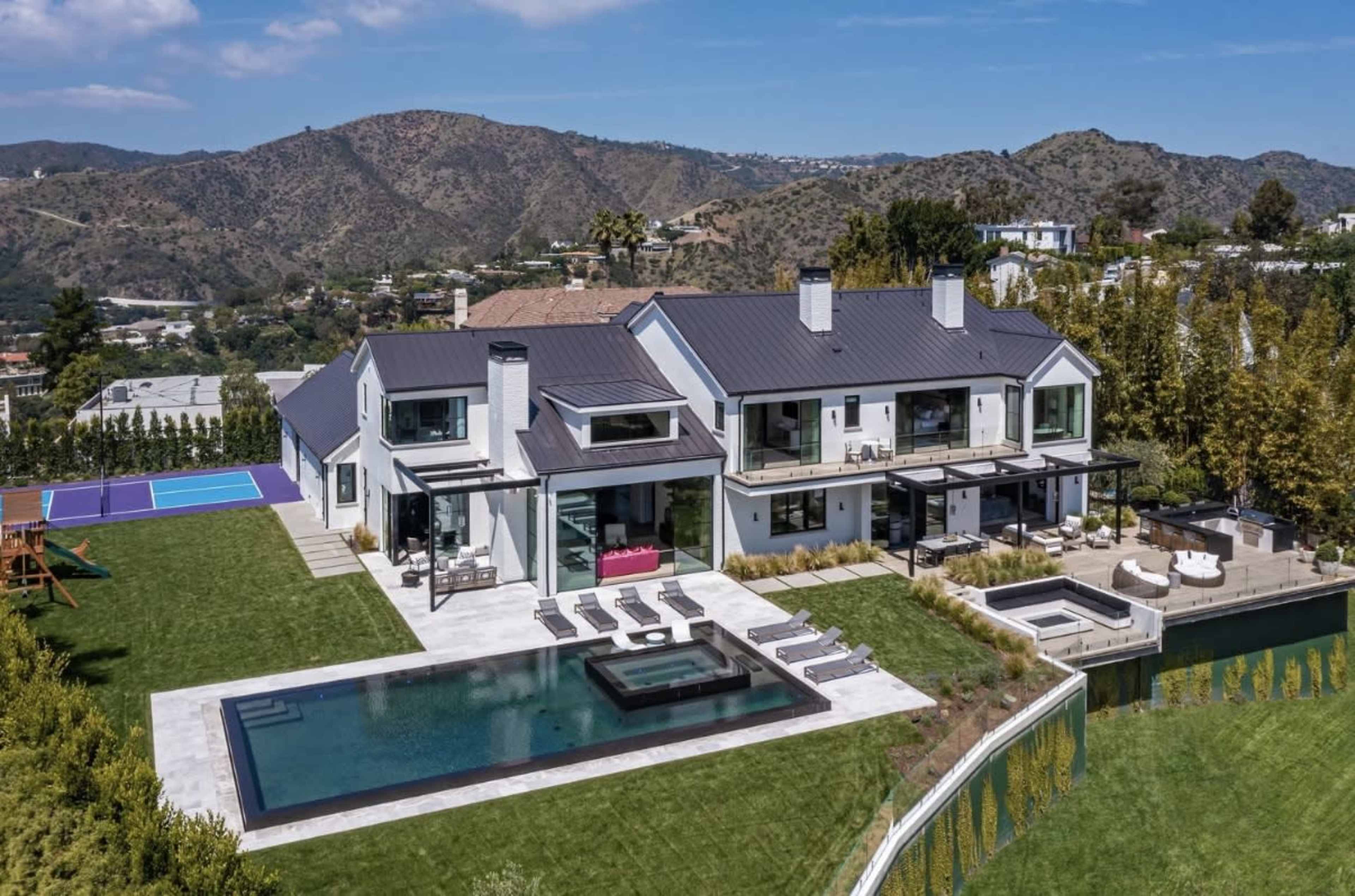 The image shows a modern two-story house with large windows, a swimming pool, and a landscaped yard, surrounded by hills and greenery.