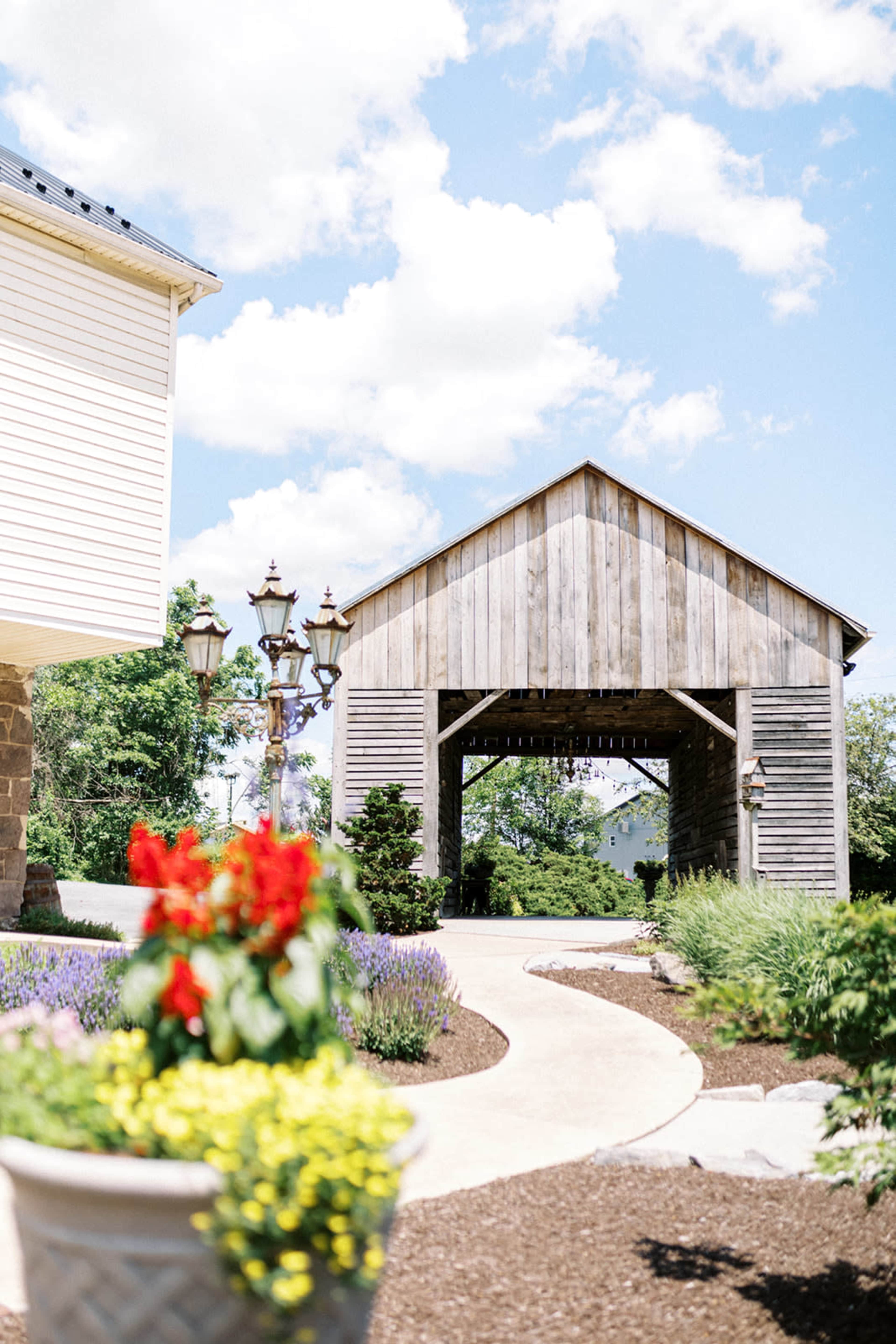 A stone pathway leads through landscaped gardens to a wooden structure under a blue sky with clouds.