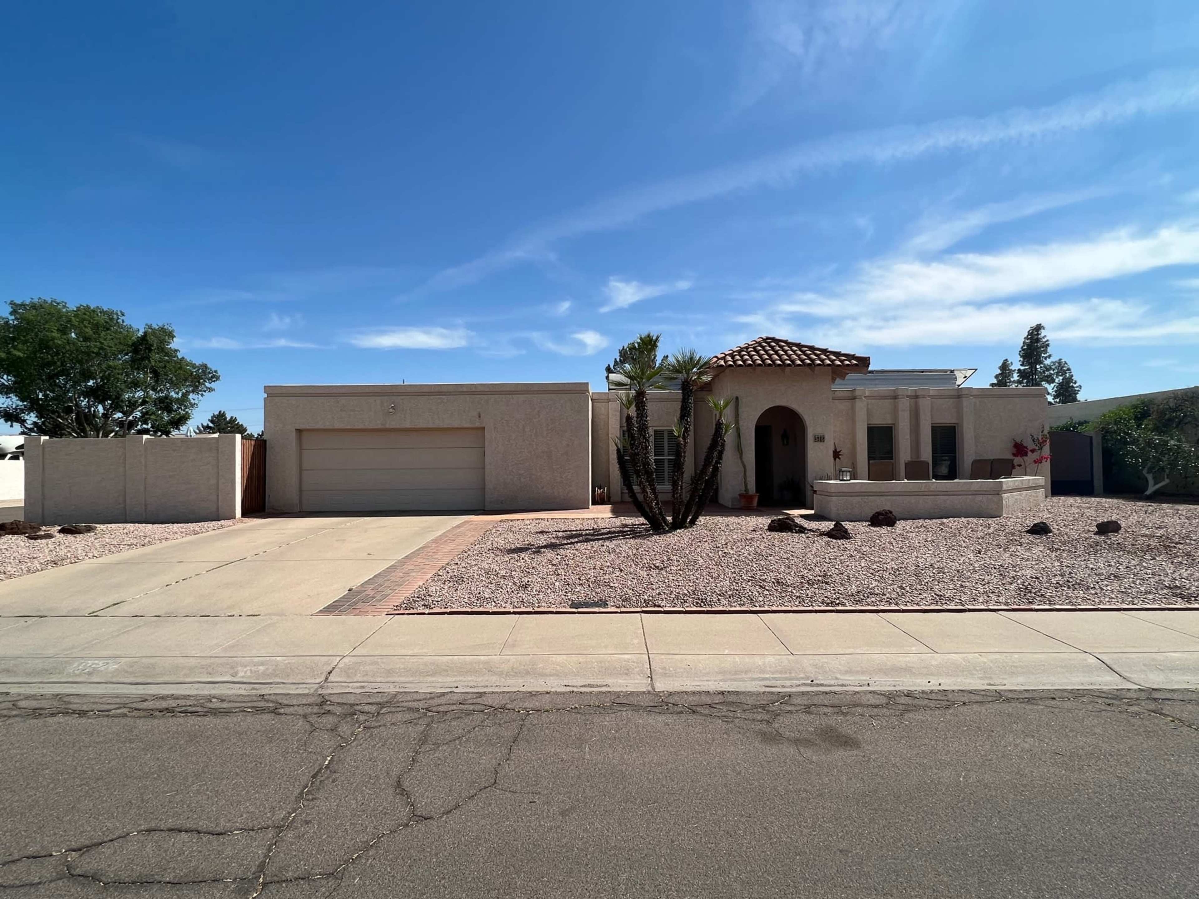 A single-story house with a tile roof, large garage, and landscaped front yard featuring gravel and desert plants.