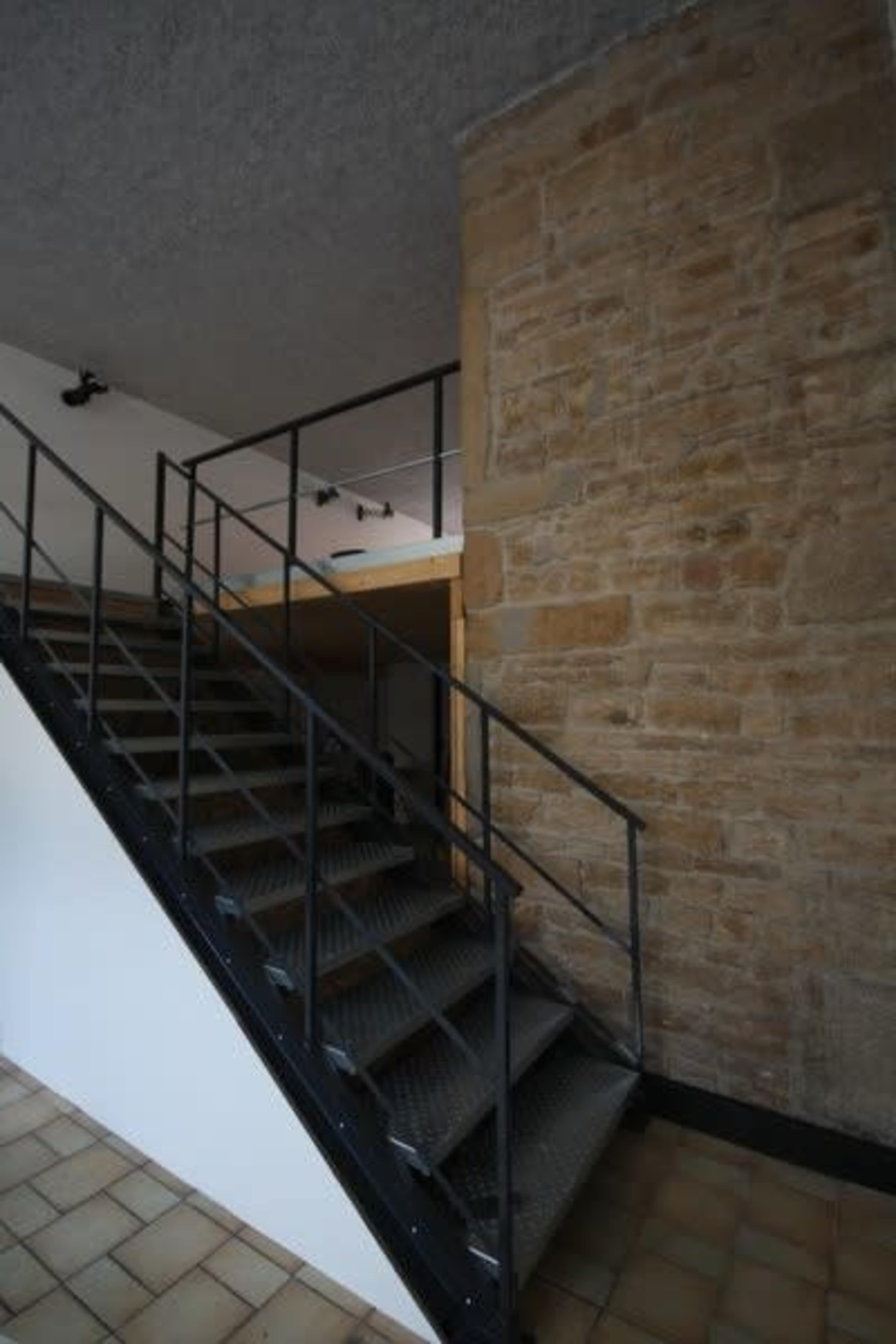 A spiral staircase with metal railings leads upward next to a textured stone wall in an interior space.