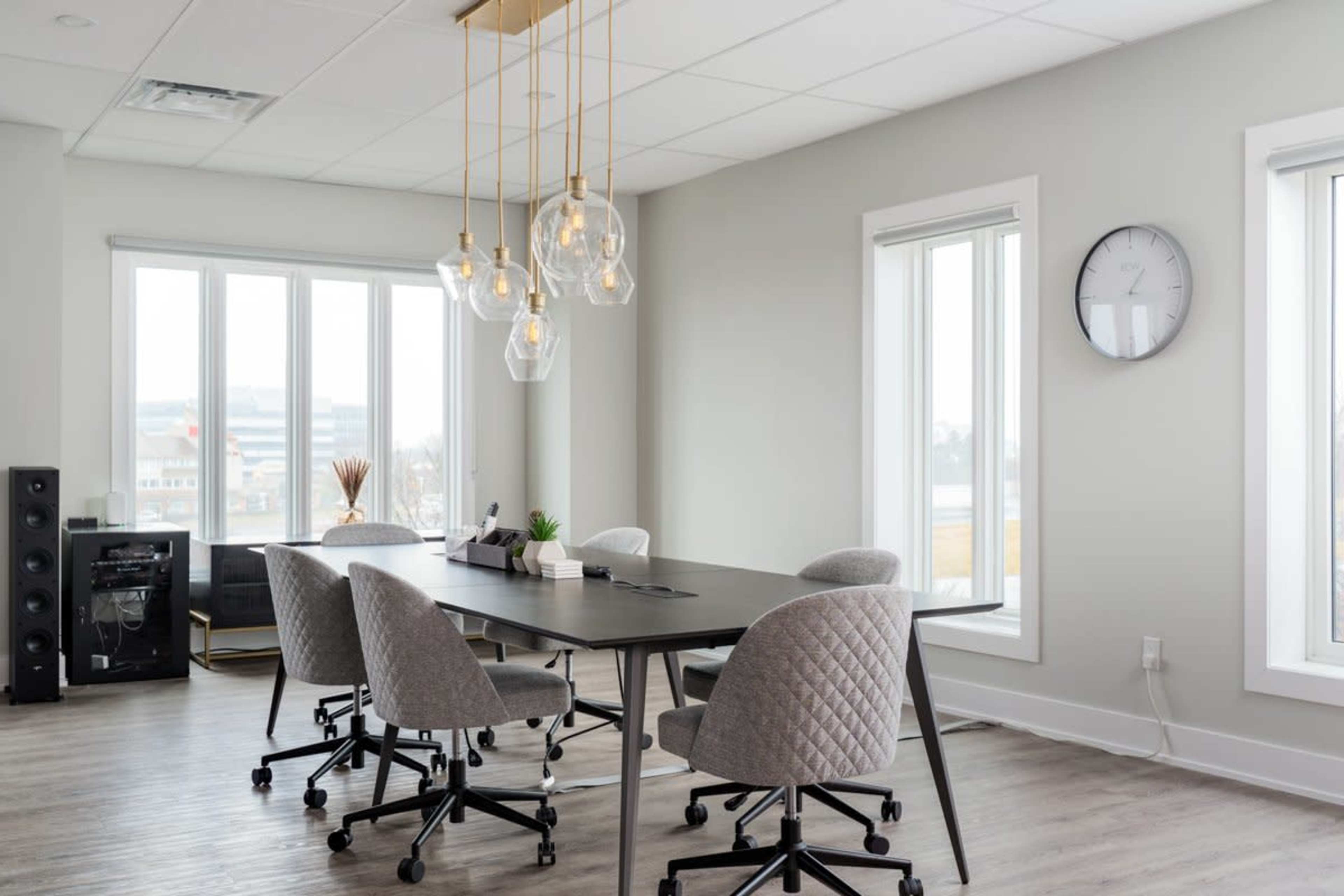 The image shows a modern conference room with a large table, four upholstered chairs, a pendant light fixture, and windows providing natural light.