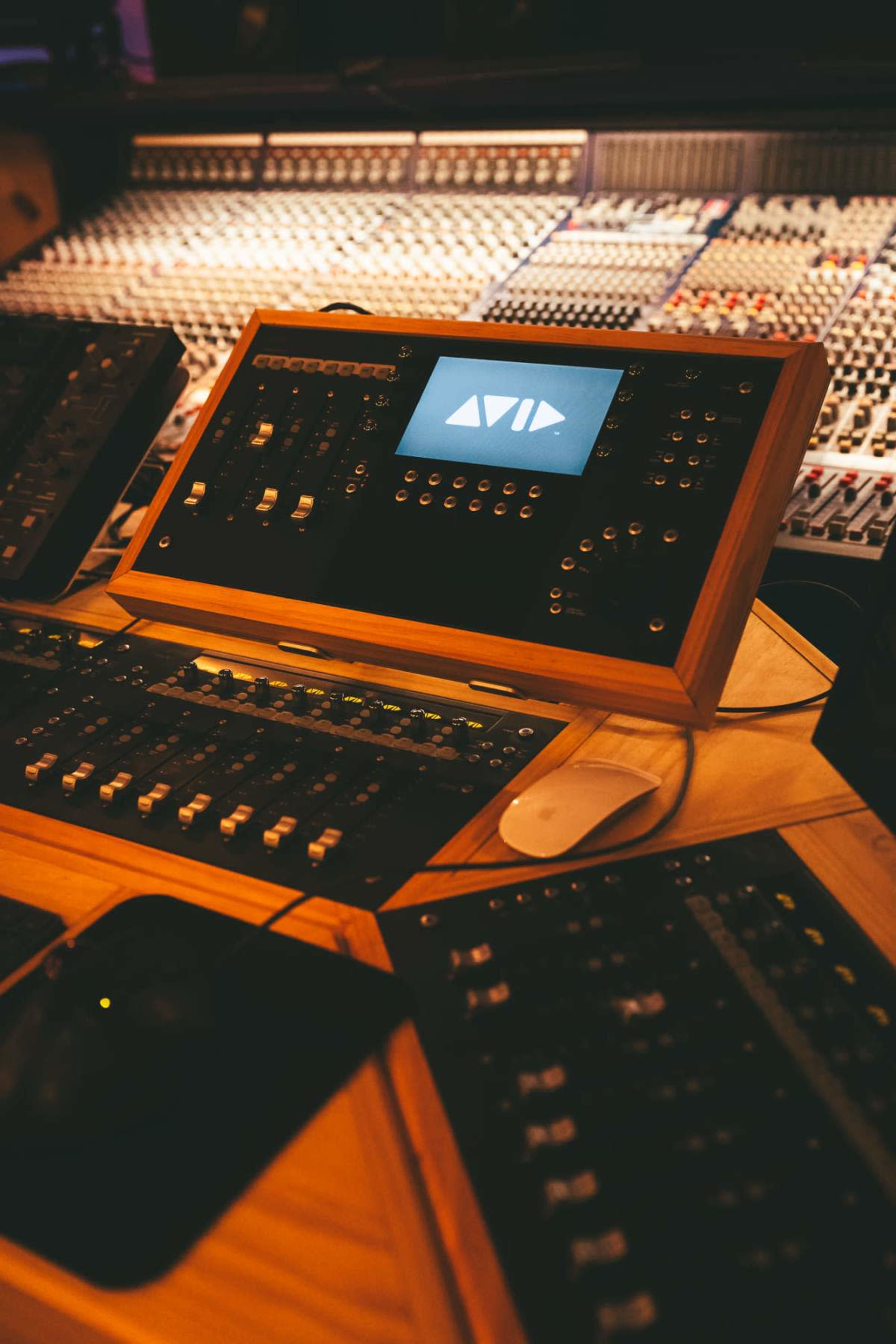 A professional audio mixing console with various buttons and sliders is prominently displayed in the foreground, while a large array of control panels is visible in the background.