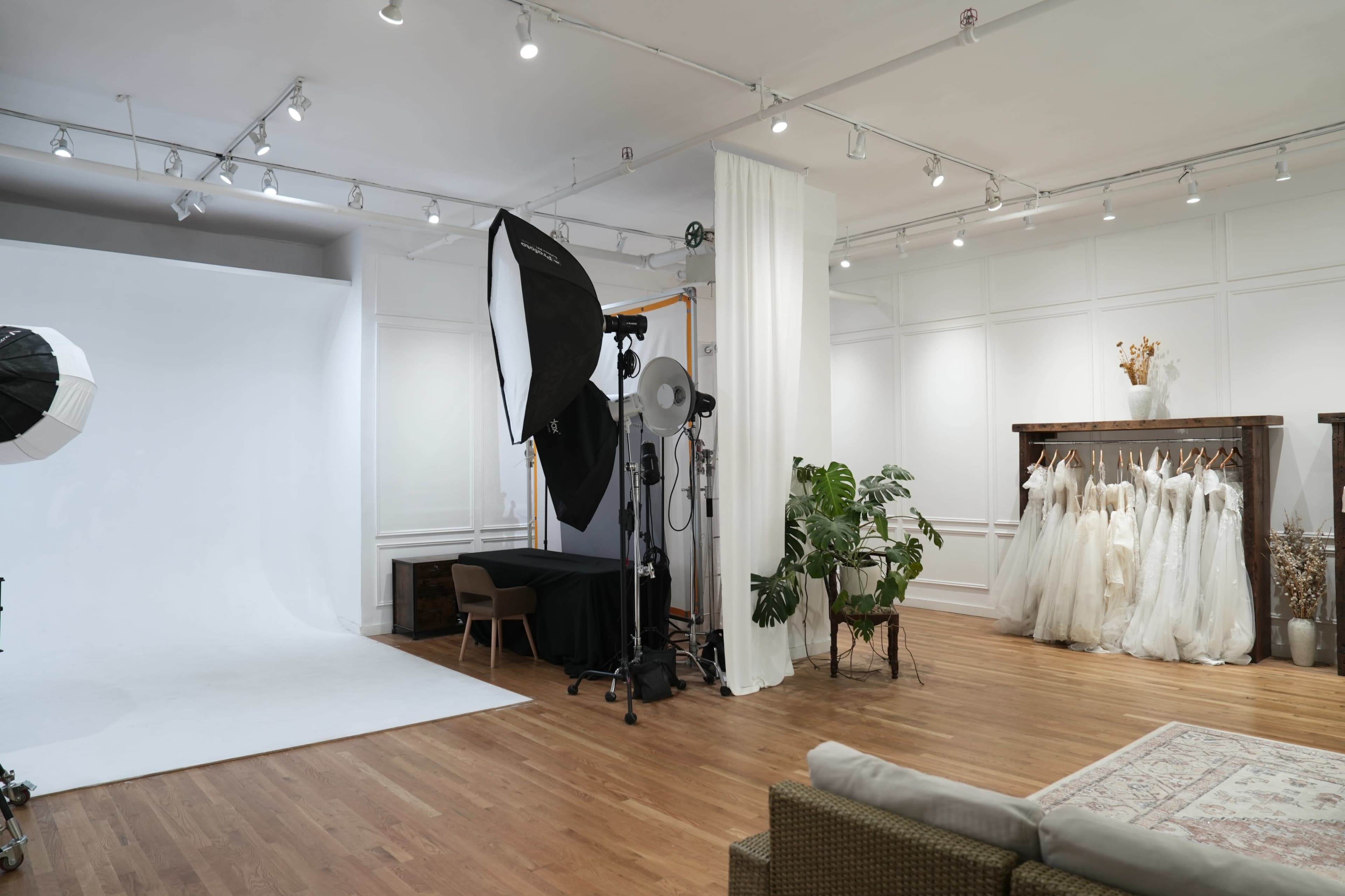 The image shows a spacious photography studio with a white backdrop, lighting equipment, and a rack of bridal dresses displayed on the right.