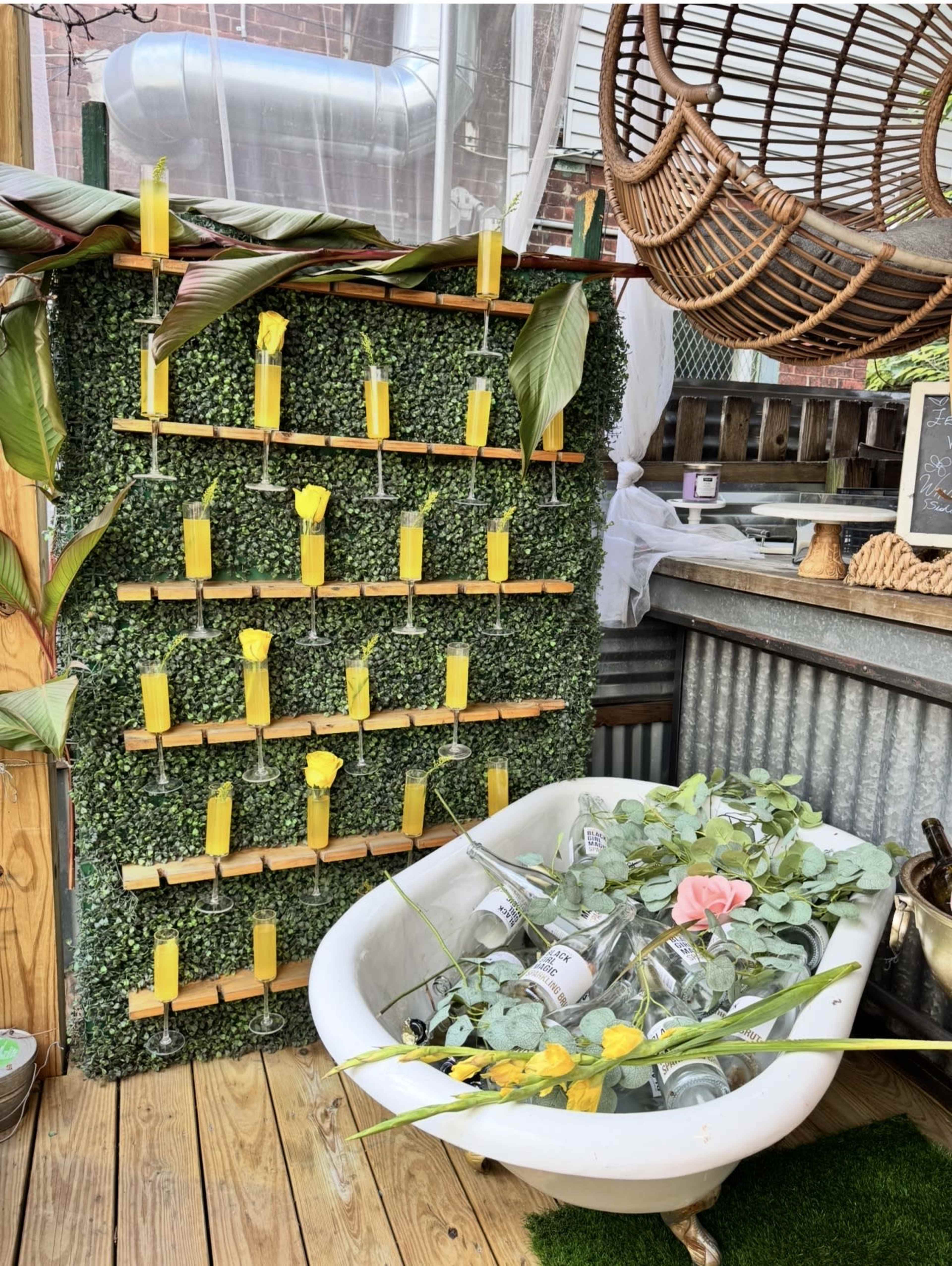 The image shows a stylish indoor space with a vertical garden on a wall, featuring yellow candles and a vintage bathtub filled with greenery and glass vases.