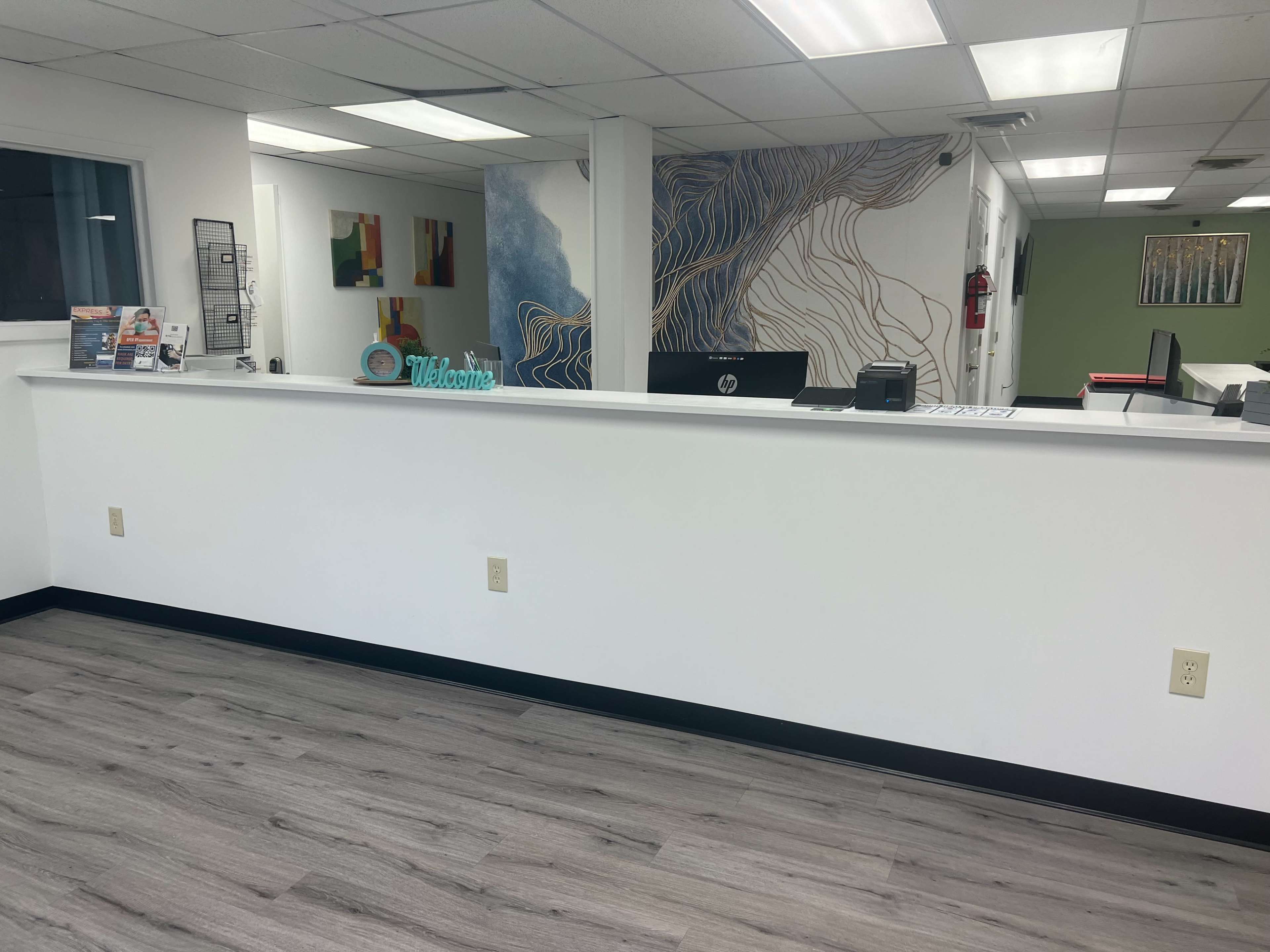 A reception area with a white counter, a computer, and decorative wall art in a professional setting.