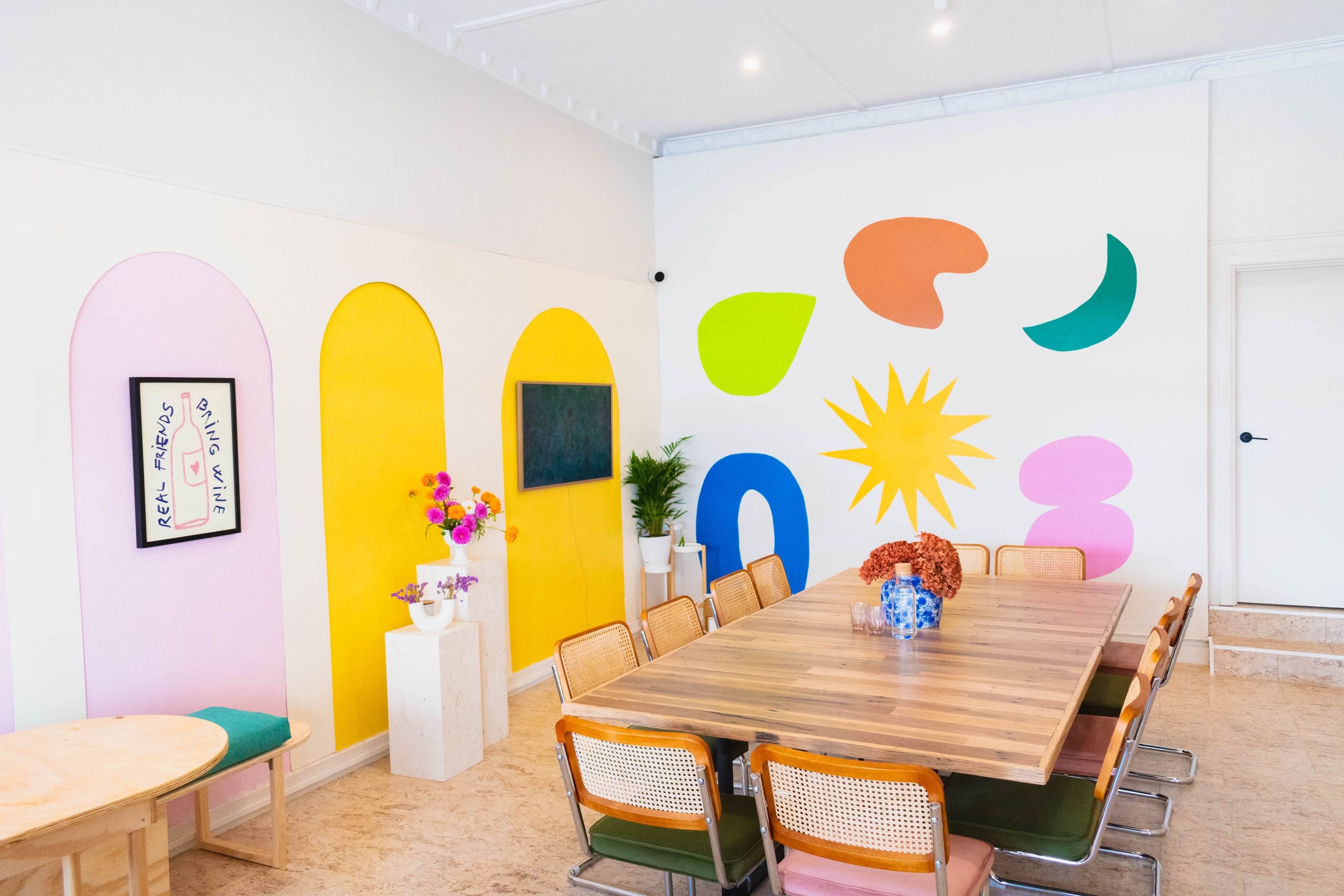 A vibrant meeting room featuring colorful wall art, a large wooden table surrounded by chairs, and decorative plants.