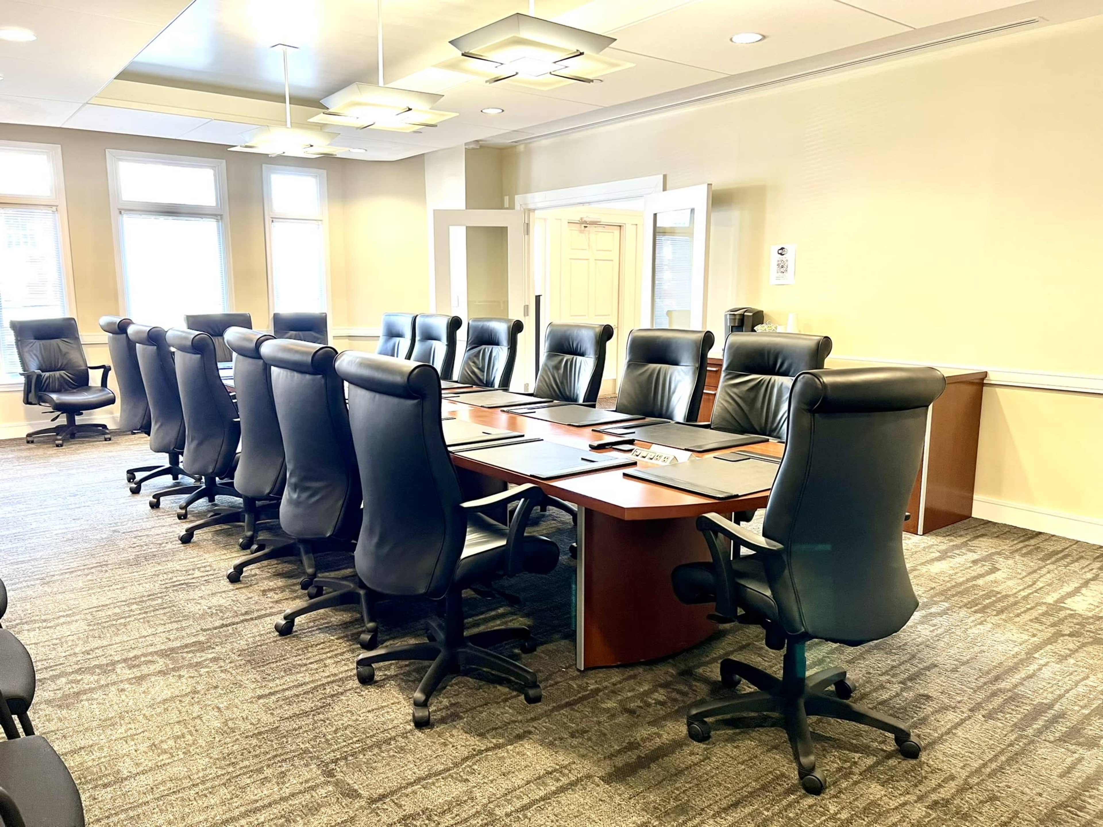 A large conference room with a rectangular table surrounded by leather office chairs and bright overhead lighting.