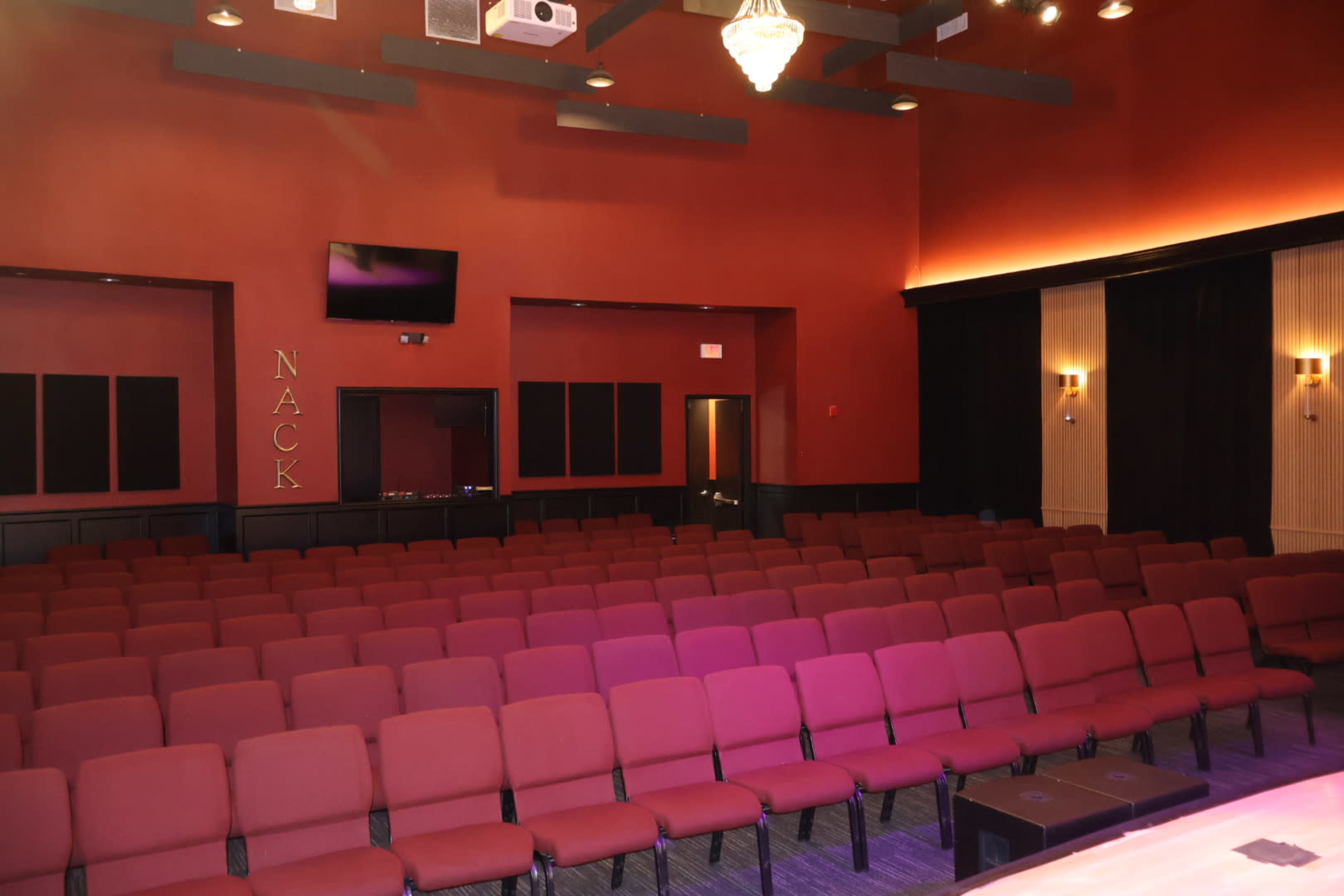 The image shows a small theater with rows of maroon chairs arranged in a deep red room, accented by a projector and wall sconces.