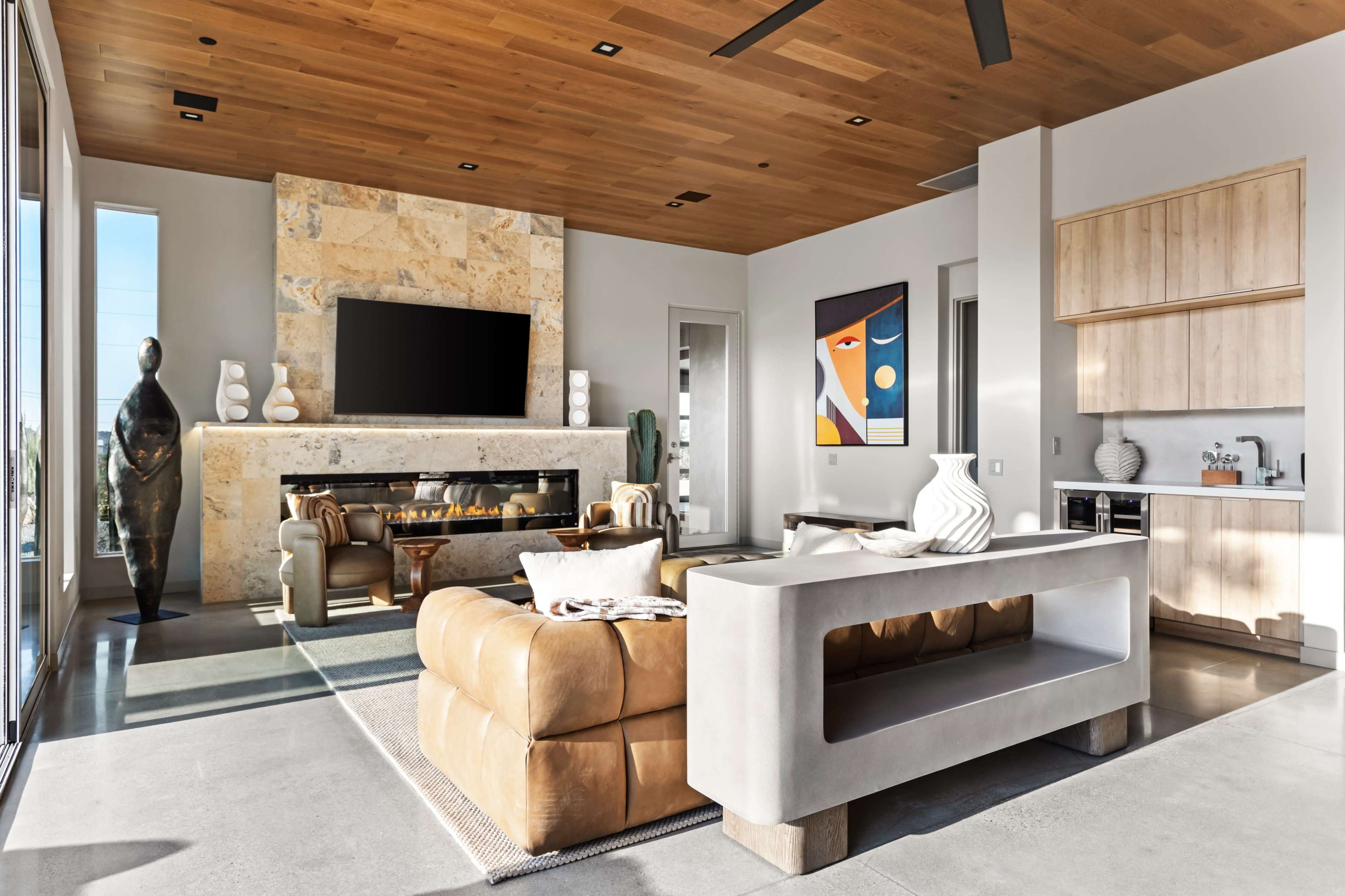 The image shows a modern living room with a stone fireplace, a large television above it, and contemporary furniture including a leather sofa and a concrete coffee table.