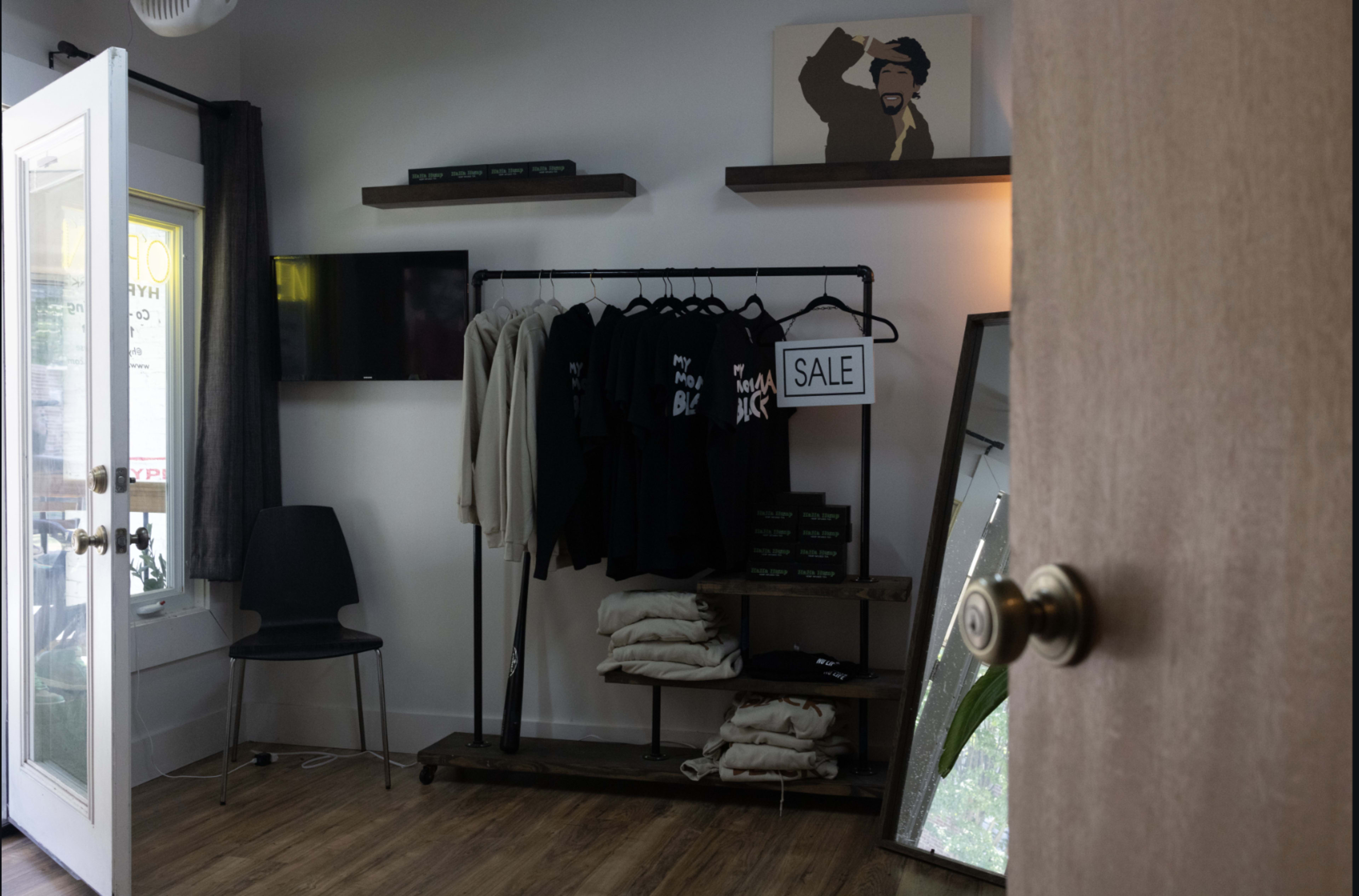 The image shows a small retail space featuring a rack of clothing with a "SALE" sign, a television on the wall, and a mirror beside it.