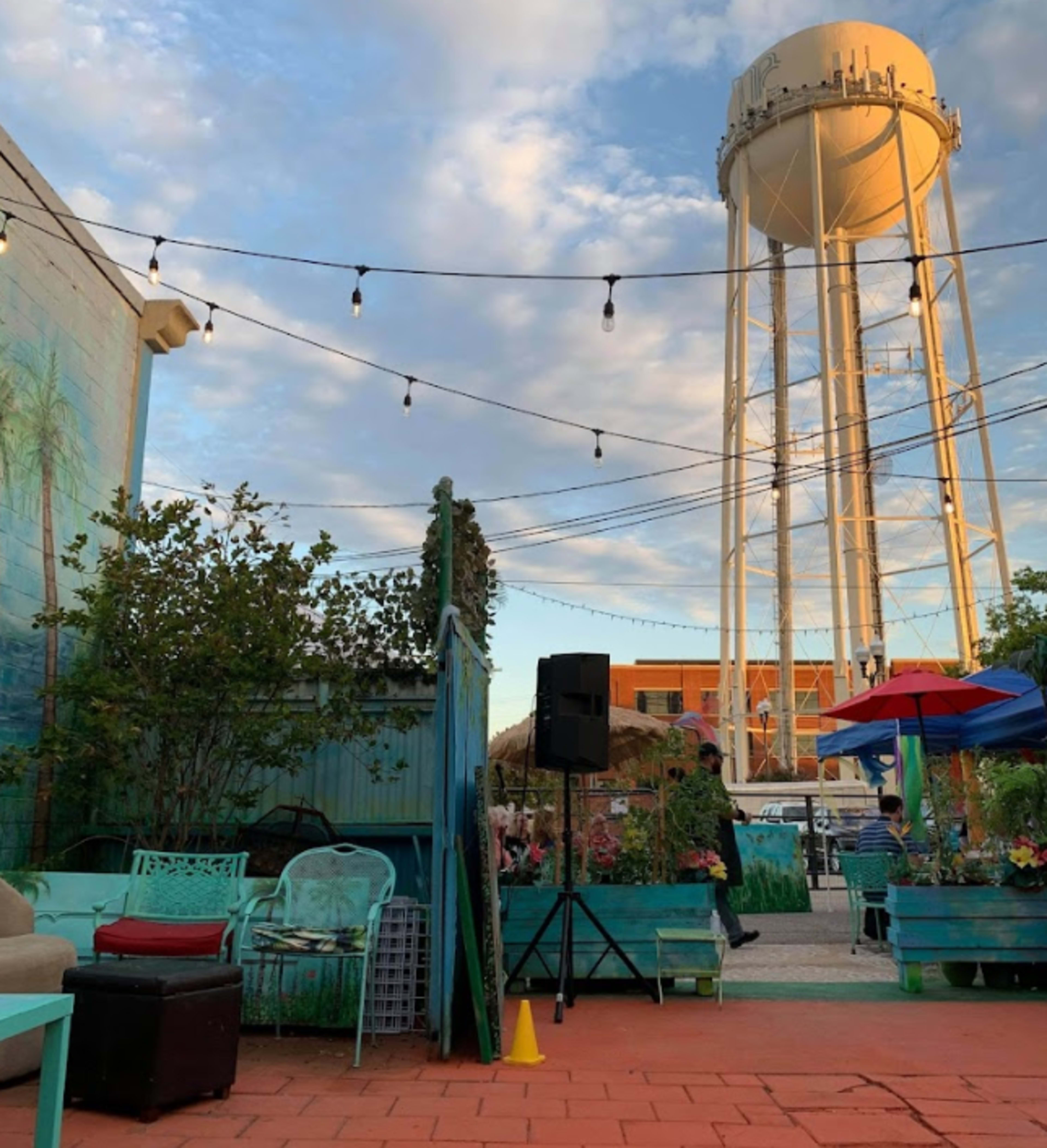 An outdoor seating area with colorful furniture, string lights overhead, and a water tower in the background.