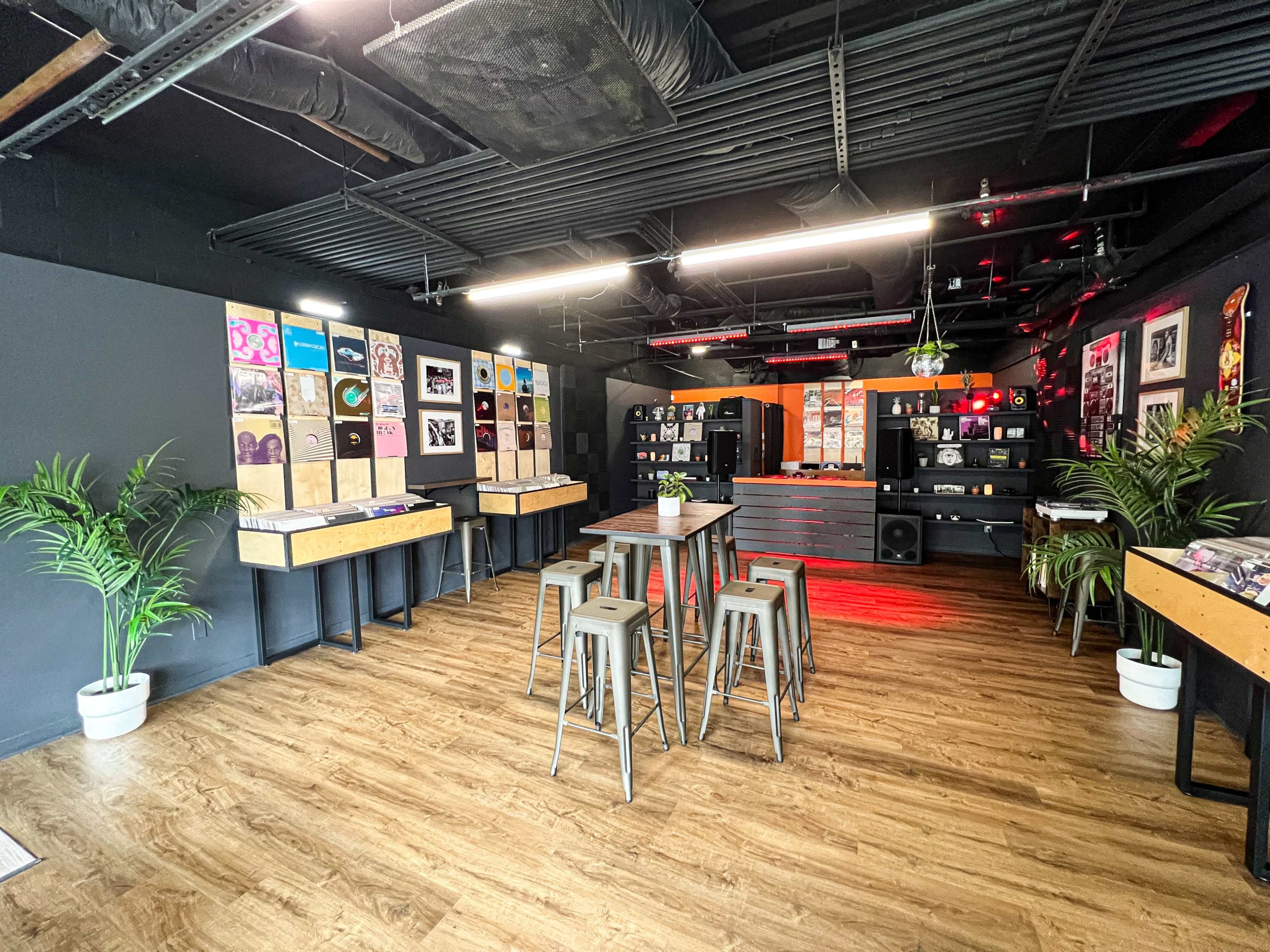 A modern interior space with wooden flooring, plants, tables, and a display of vinyl records on the walls.