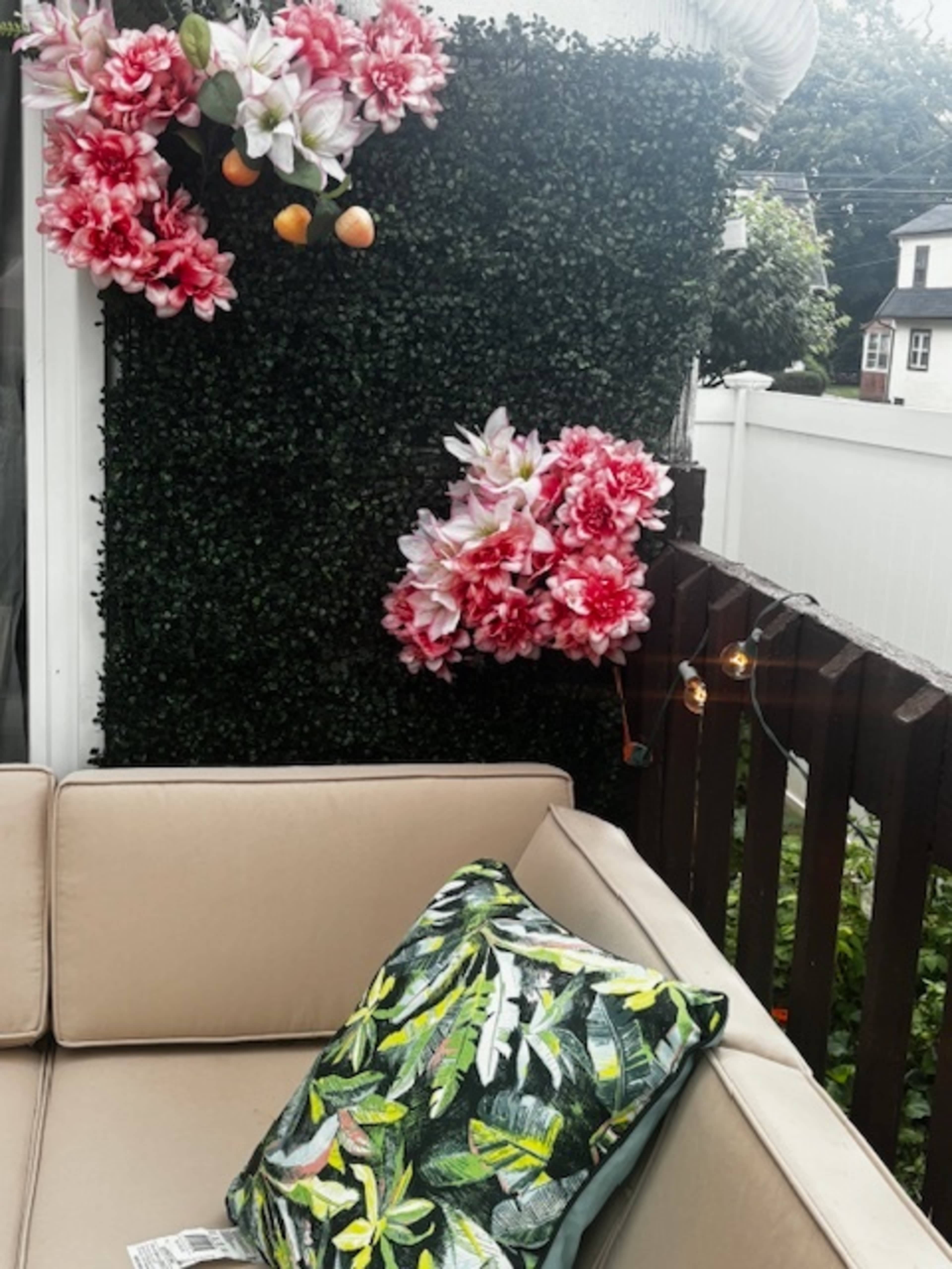 A sofa with a decorative leaf-patterned pillow sits adjacent to a wall adorned with artificial flowers and greenery.